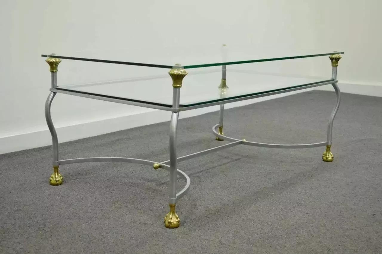Vintage Maison Jansen Style Brass Brushed Steel & Glass Ball and Claw Foot Coffee Table. Item features two tiers of glass, brass accents, stretcher supported base, and ball in claw form feet. The table is stamped 