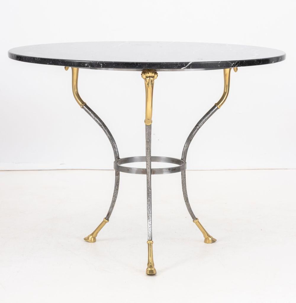 Gueridon in ottone e ferro battuto in stile Maison Jansen, con piano in marmo nero circolare sopra una struttura in ferro circolare con teste di bue in ottone che terminano con tre piedi a zoccolo. 27