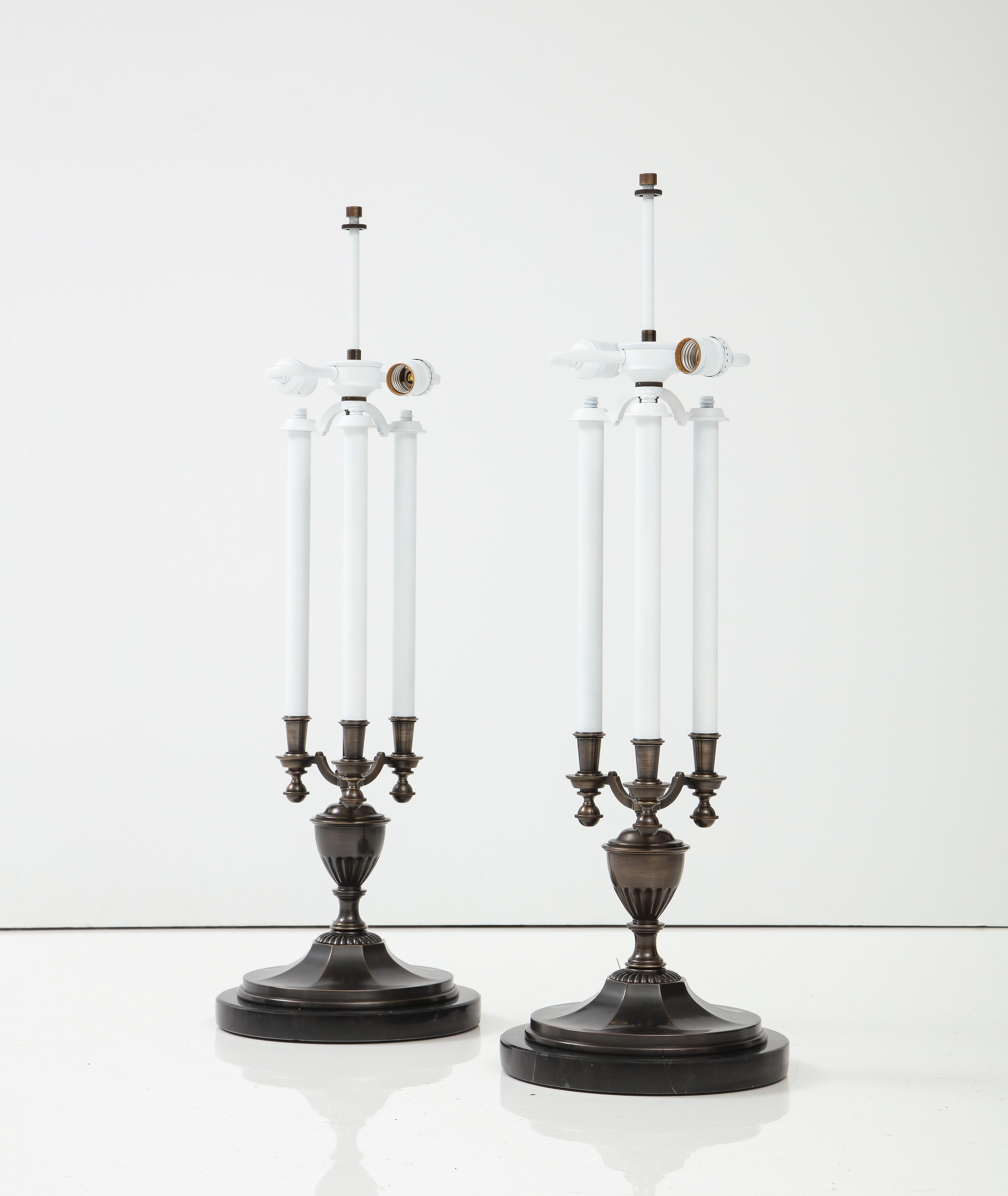 Traditional candelabra style lamps an a modern bronze finish. Each lamp has 3 enameled metal candles with sockets using candelabra type bulbs. Lamps sit on black marble disc bases. Rewired for use in the USA.