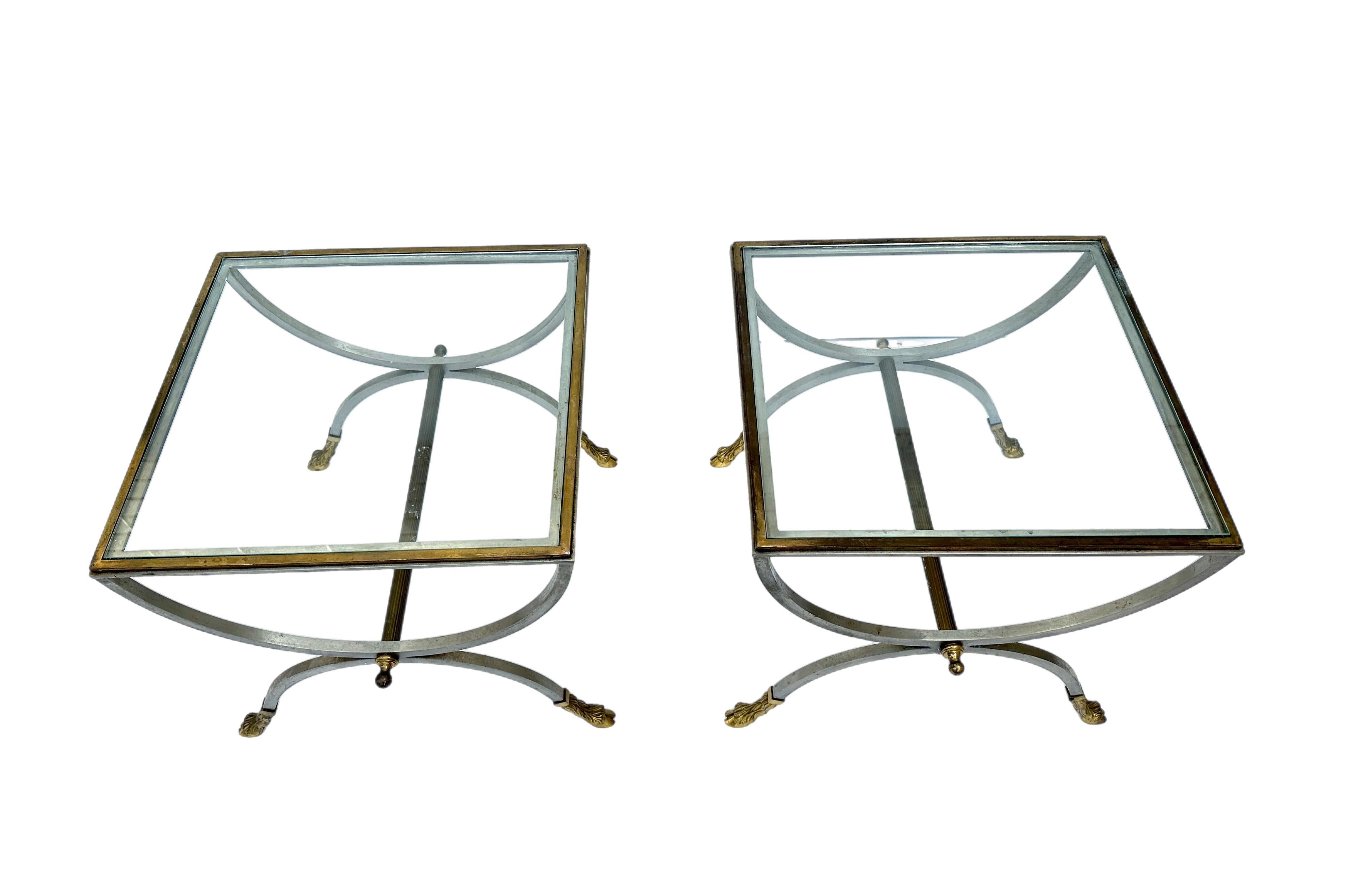 Maison Jansen style neoclassical brushed steel and brass tables, a pair.
Curule form with cloven hoof feet.
Stamped Made in Italy.
Some light typical wear, needing polishing.
New glass.
