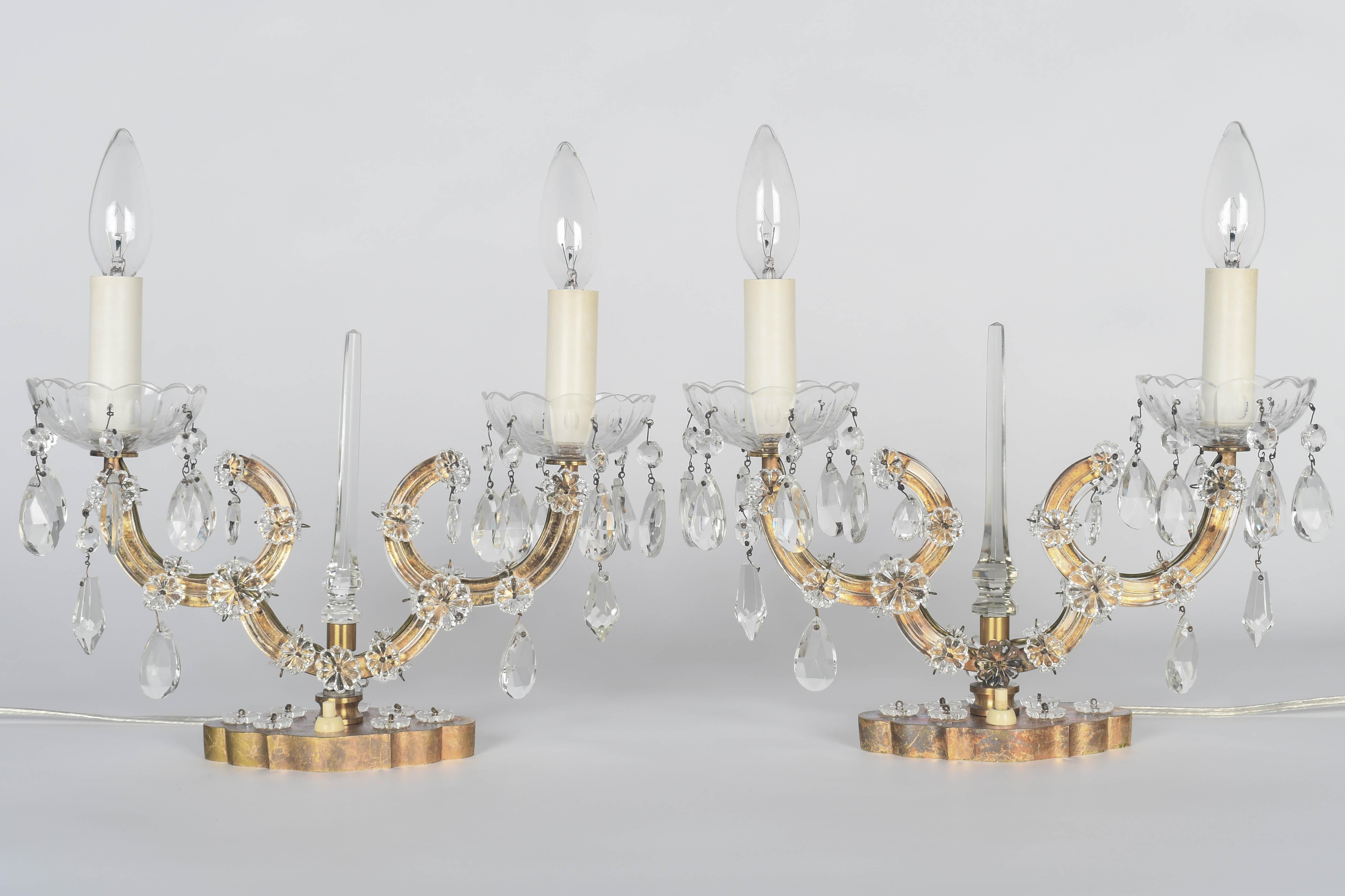 A pair of Mid Century French Maison Jansen style Marie Therese two-light crystal girandoles, or table lamps. Gold tone scrolled arms with glass bobeches. Brass base with crystal rosettes. Rewired with new sockets and candle covers. Circa 1950s.