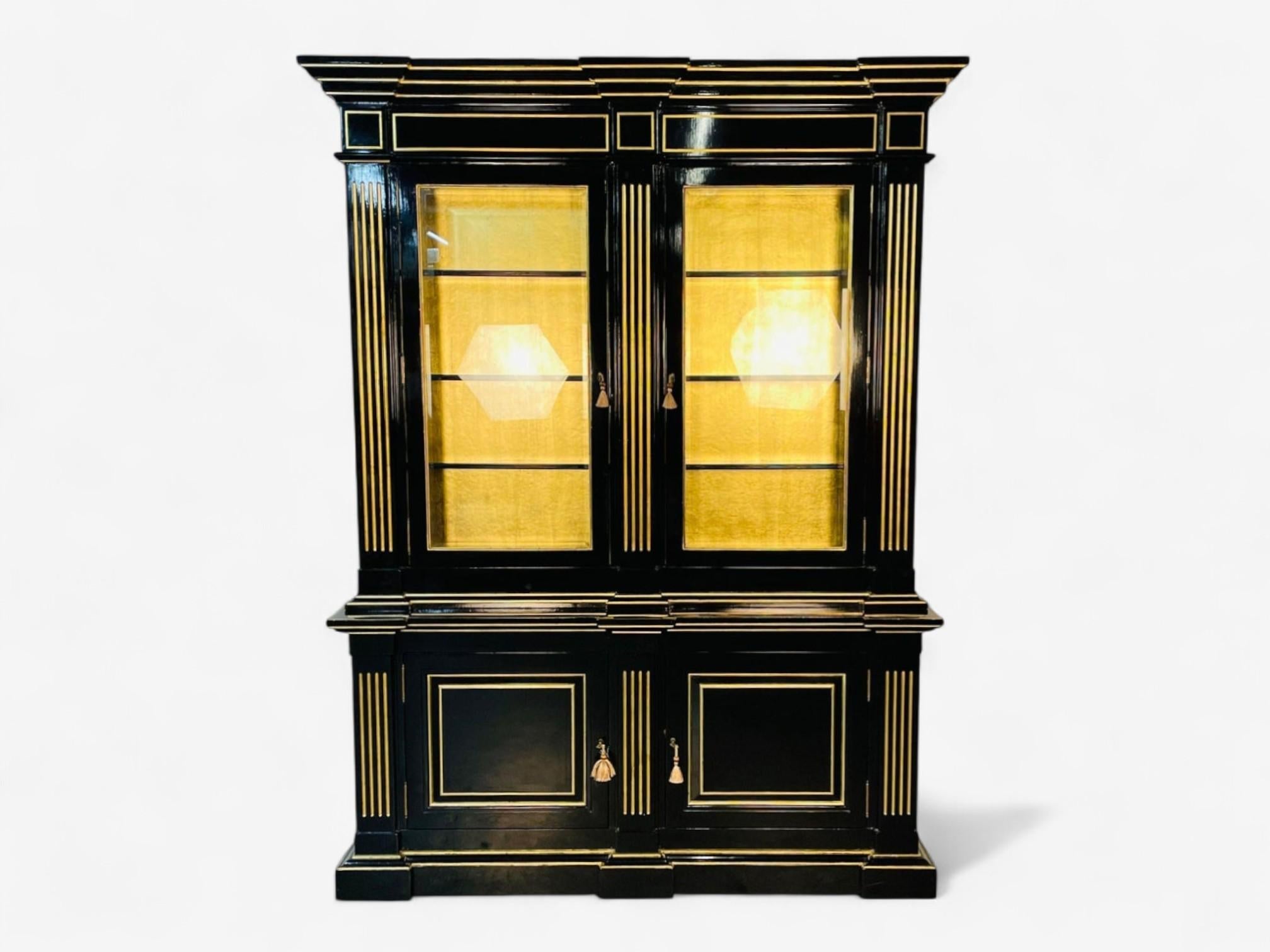 Libreria/armadio in stile Hollywood Regency Maison Jansen, ebano, foglia d'oro
 
Uno splendido mobile rifinito con due ante in vetro smussato che si aprono su un supporto in foglia dorata e un interno illuminato. Il piano sottile e slanciato, con un