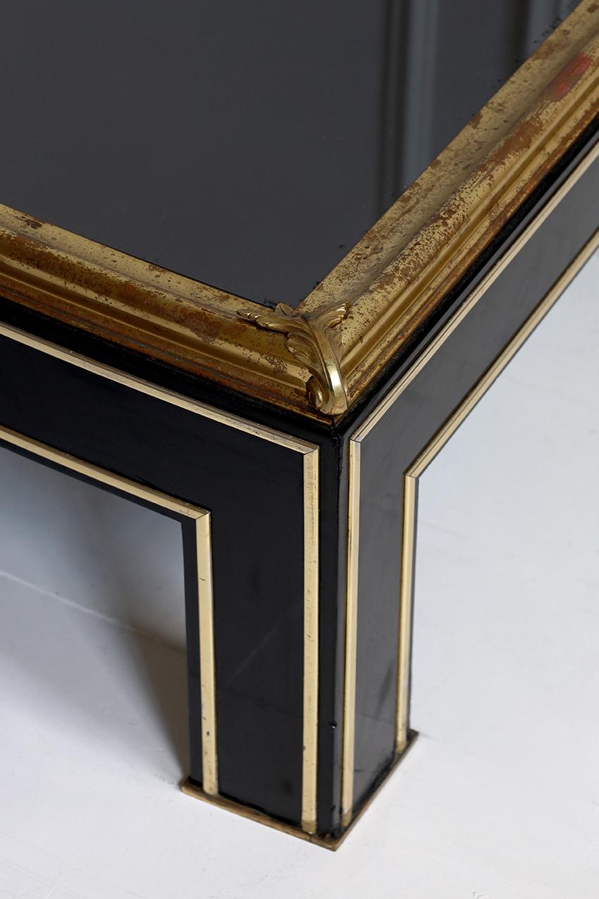 An exceptionally elegant square coffee table in the style of Maison Jansen, dating to the 1970s. The architectural frame is finished in deep black lacquer with polished brass detailing, and is topped with a sleek black mirrored glass surface.  A