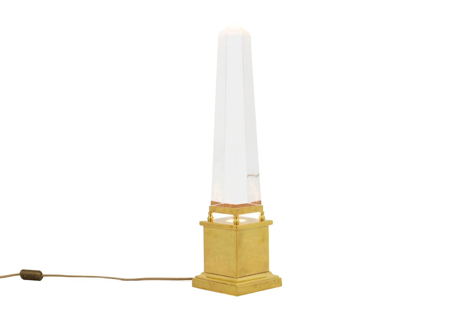 Sandro Petti for Maison Jansen, in the style of.

Obelisk lamp in Lucite standing on a cubic gilt brass base opened in its centre to let pass the light, finished by a molded square base and topped by a small base on four legs supporting the