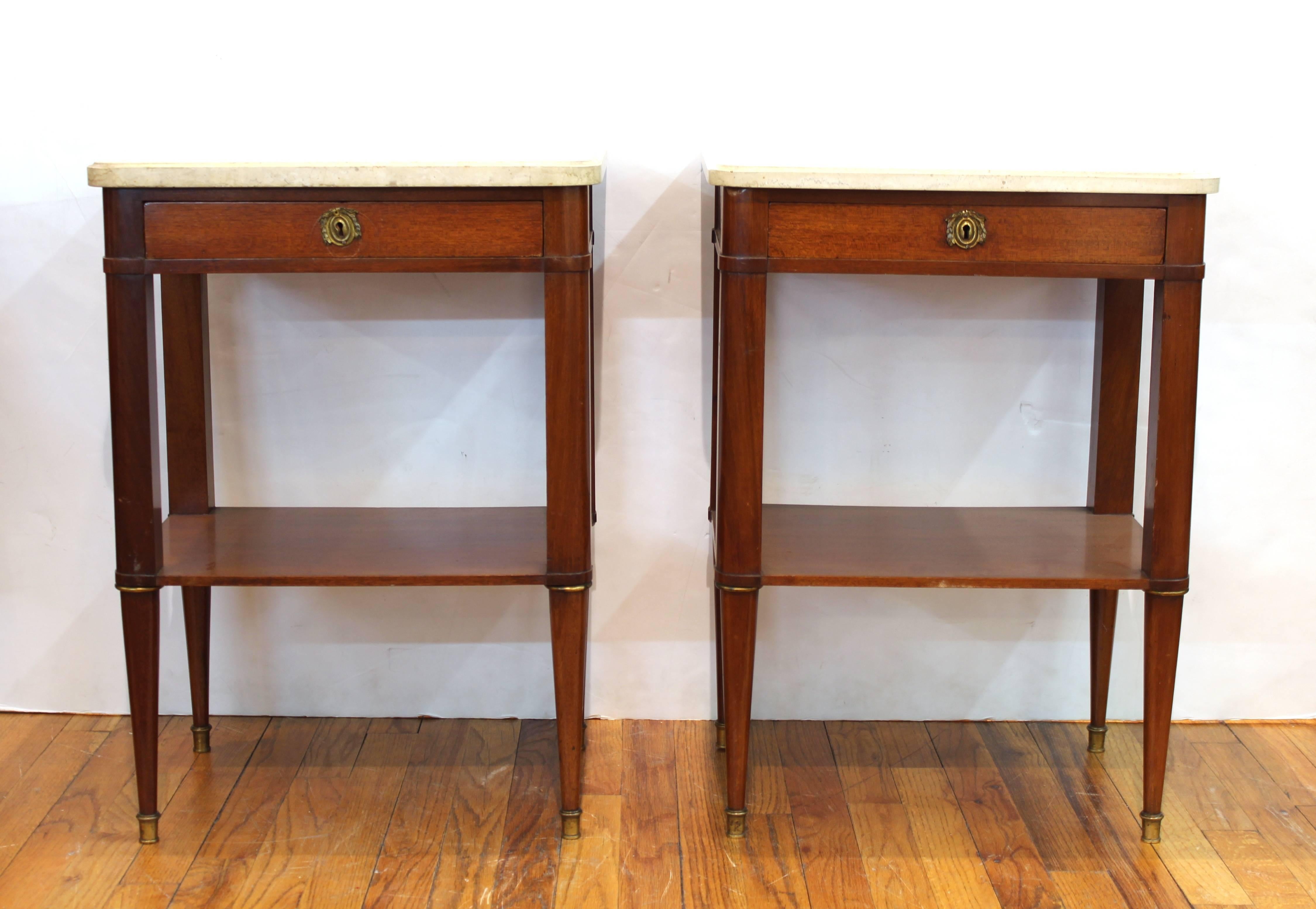 A pair of Maison Jansen style nightstands or end tables in mahogany with marble tops. The pair was made in France and is in Louis XVI style. Each one has a support shelf on the lower level and a single centre drawer underneath a marble-top. In good