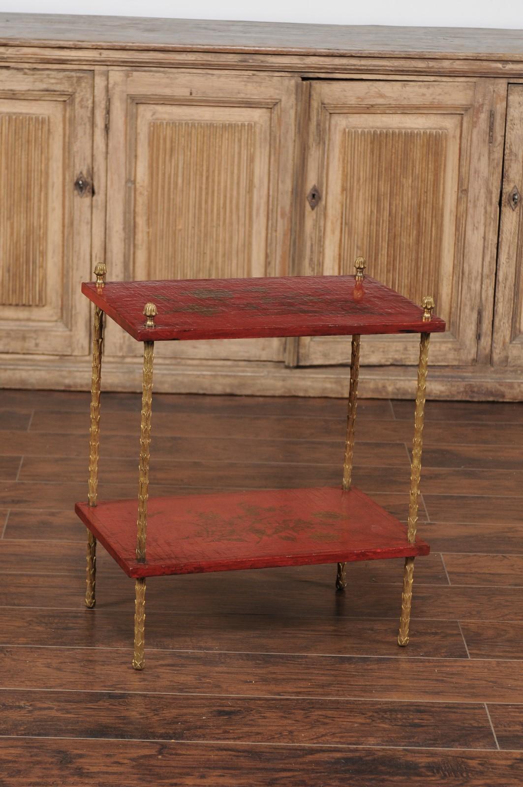 A French vintage Maison Jansen style tiered side table from the mid-20th century, with bronze legs and chinoiserie décor. This French Maison Jansen style table features four slender bronze legs with foliage style texture, supporting and securing two