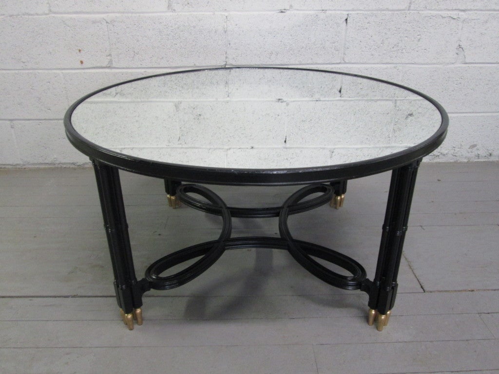 Maison Jansen style coffee table with a mirrored top. Black legs and a decorative scrolled stretcher with gold feet.