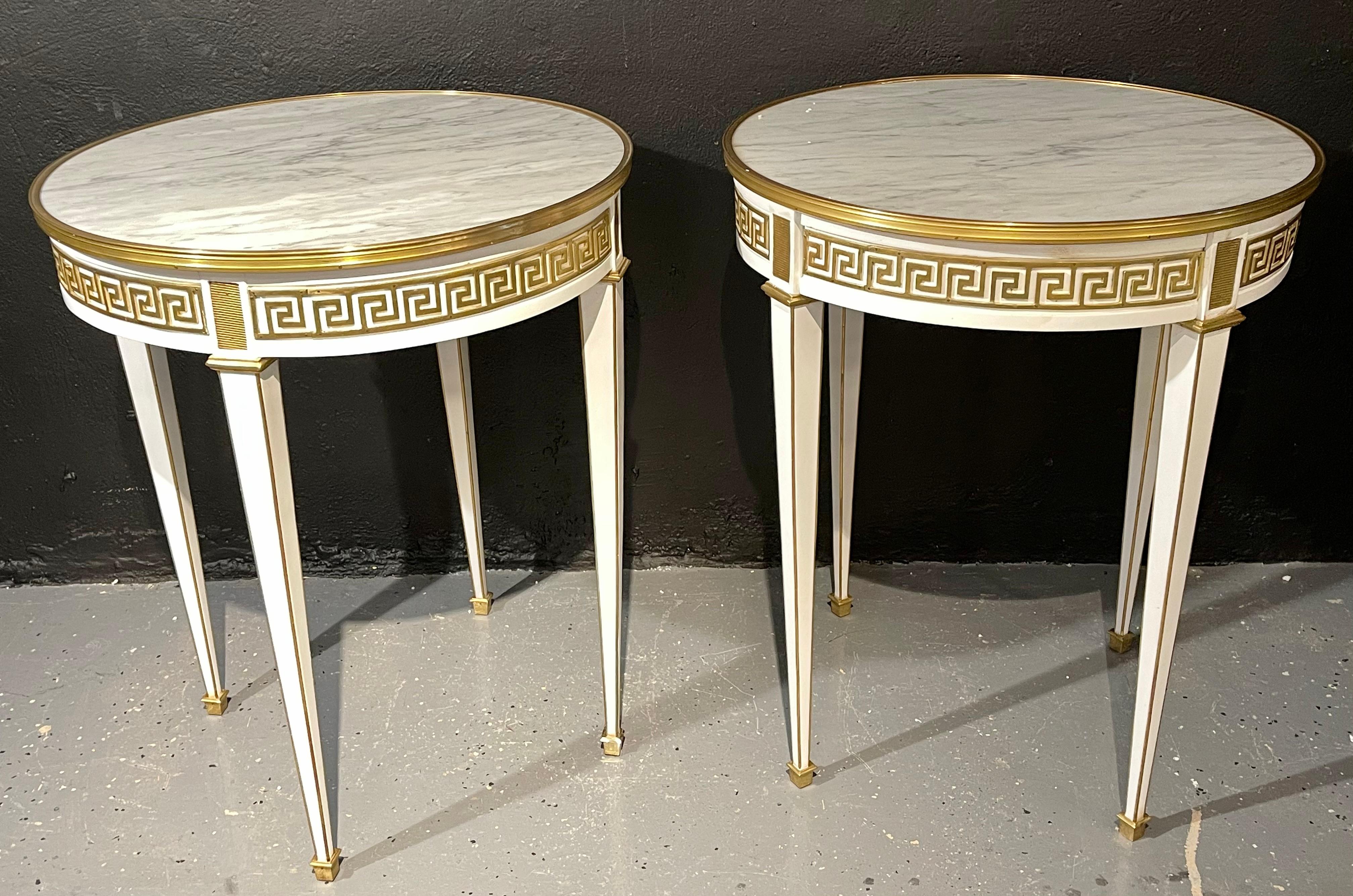 Pair of Bouillotte / end tables. Each having bronze framed white marble tops supported a white base with a Greek key designed bronze apron having cookie cutter bronze corners. The whole having one-drawer over sleek and stylish bronze framed tapering