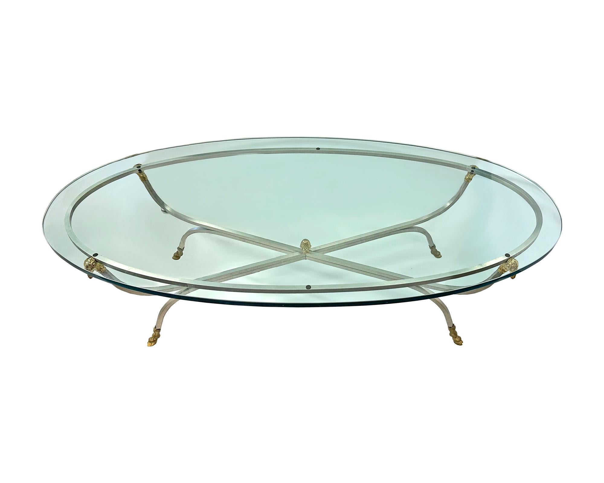 An oval coffee table on a metal base in the style of Maison Jensen. The metal base features small brass ram heads at the top of each leg and brass ram hooves at the foot of each leg. The underside of one hoof is marked 