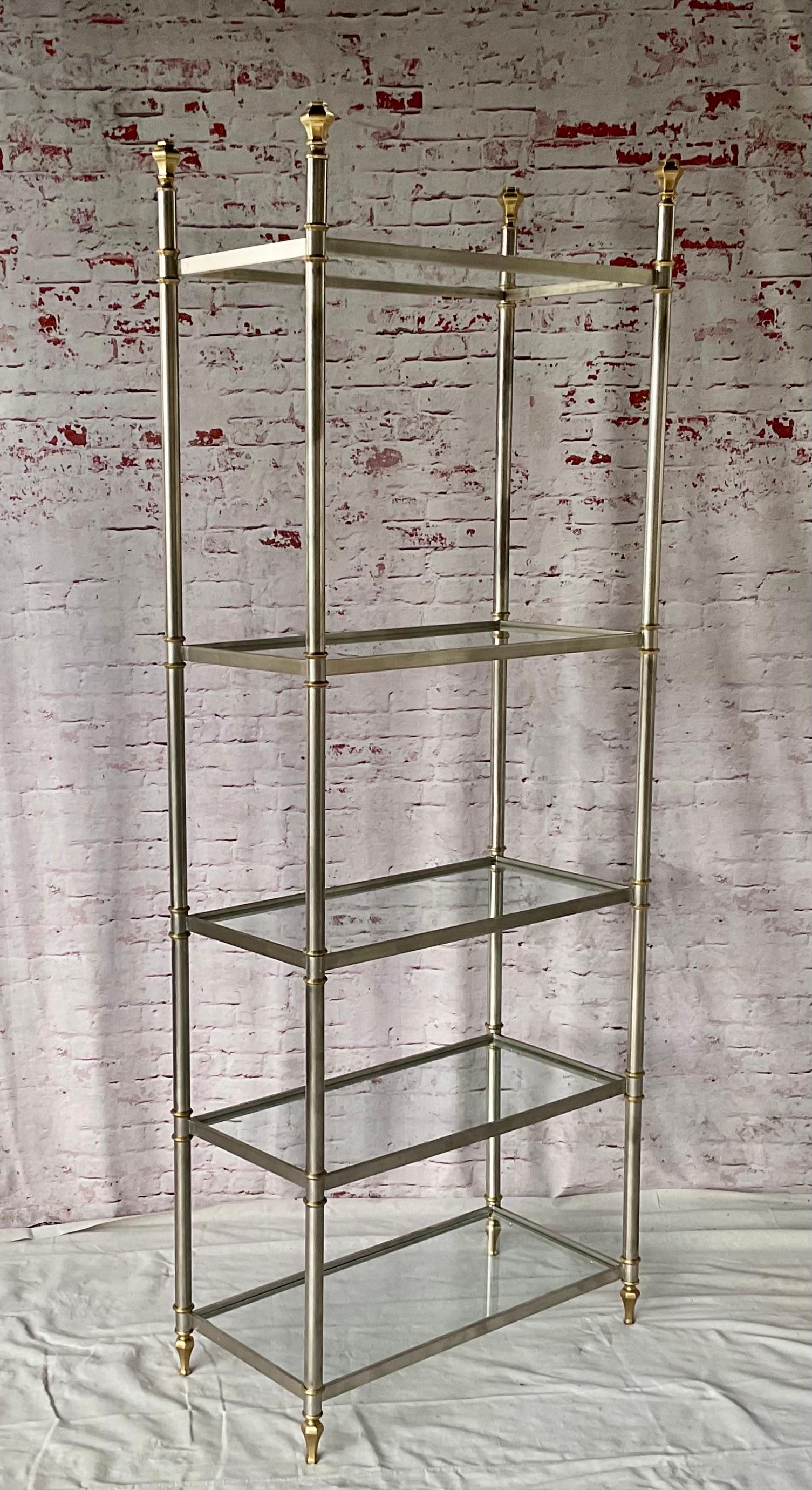  Etagère en acier brossé et laiton avec cinq étagères en verre, style Maison Jansen du milieu du 20e siècle. Le design haut incarne la sophistication élégante du style de la Maison Jansen, mélange de glamour classique et moderne. Il s'agit d'une