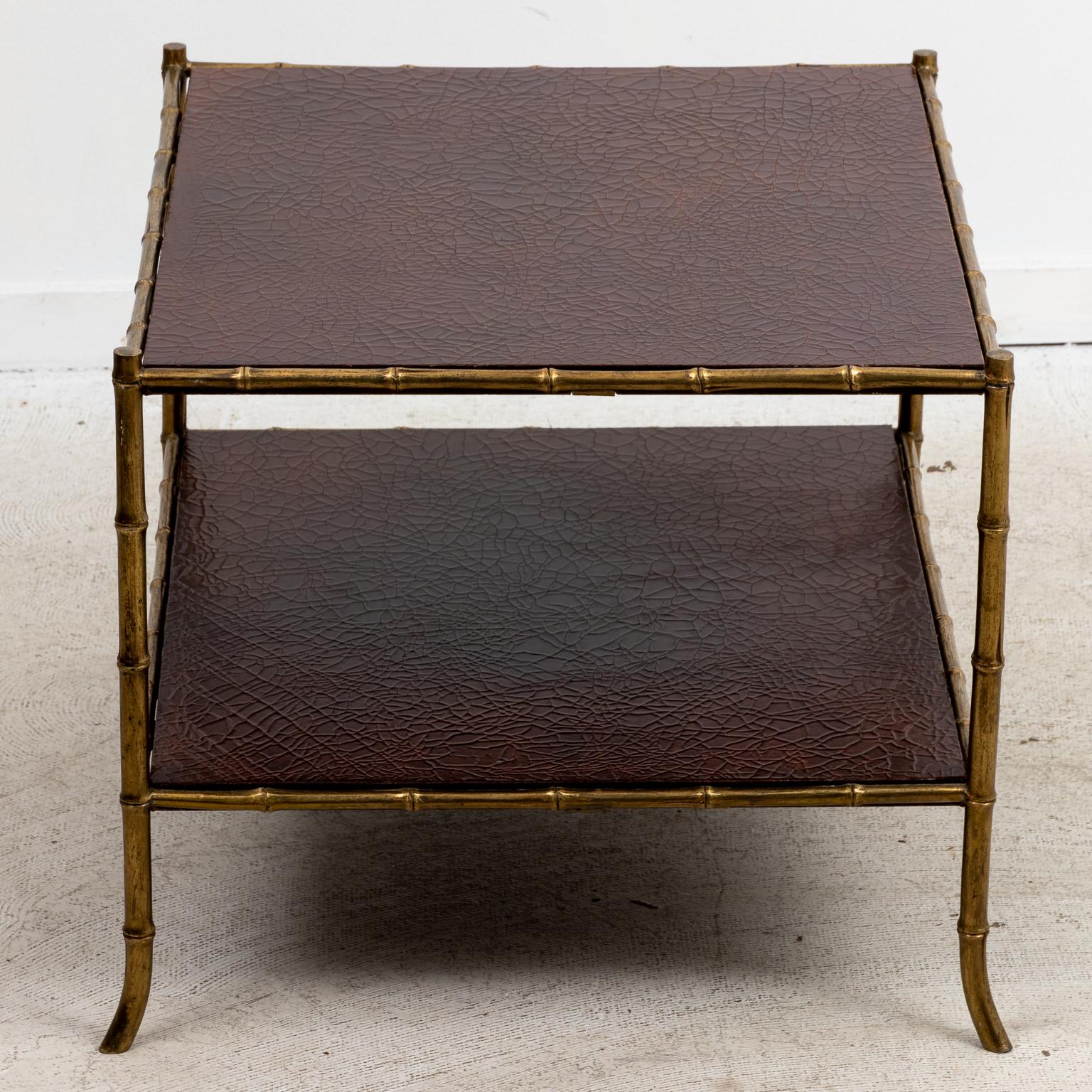 Circa 1940s Maison Jansen attributed brass and brown leather two tiered end table in the French Empire style with faux bamboo brass legs. Made in France. Please note of wear consistent with age including minor brass tarnish as seen on the feet.