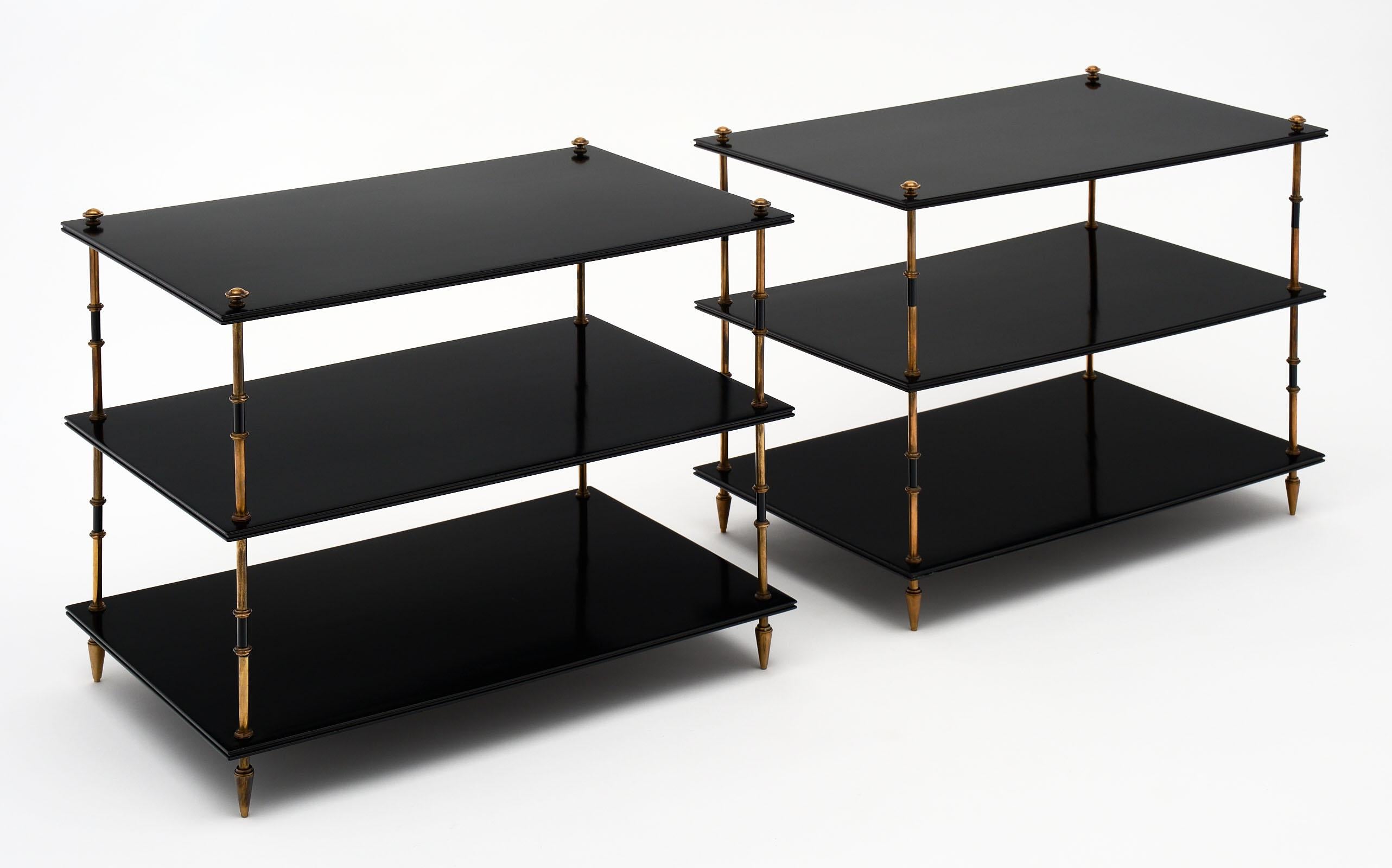 Pair of three-tiered side tables by Maison Jansen. This pair has been ebonized and finished with a lustrous French polish. The shelves are separated by solid brass and lacquered steel sections and are supported on gilt brass toupee feet.