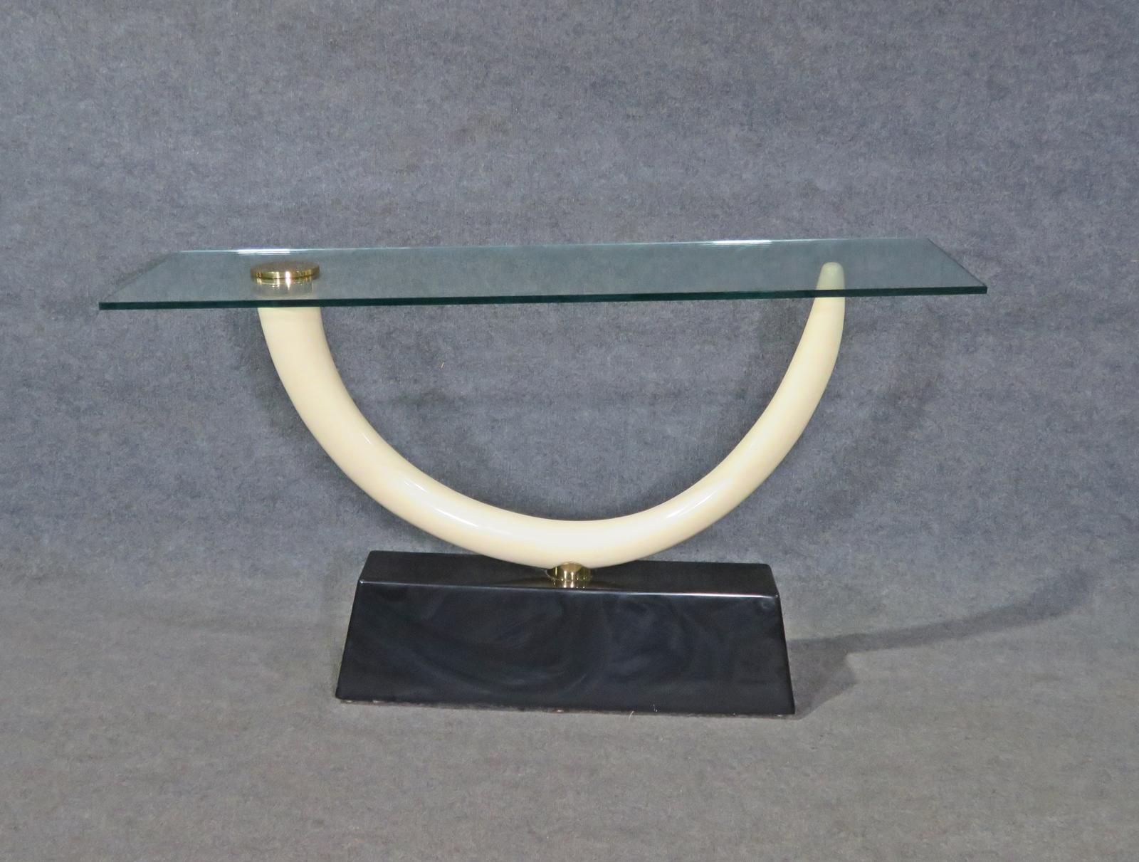 This is an iconic Maison Jansen Tusk form console table with a gorgeous resin tusk and glass top with a brass and a black ebonized base. The table is in very good condition but will show signs of use such as minor surface scratches on the top and