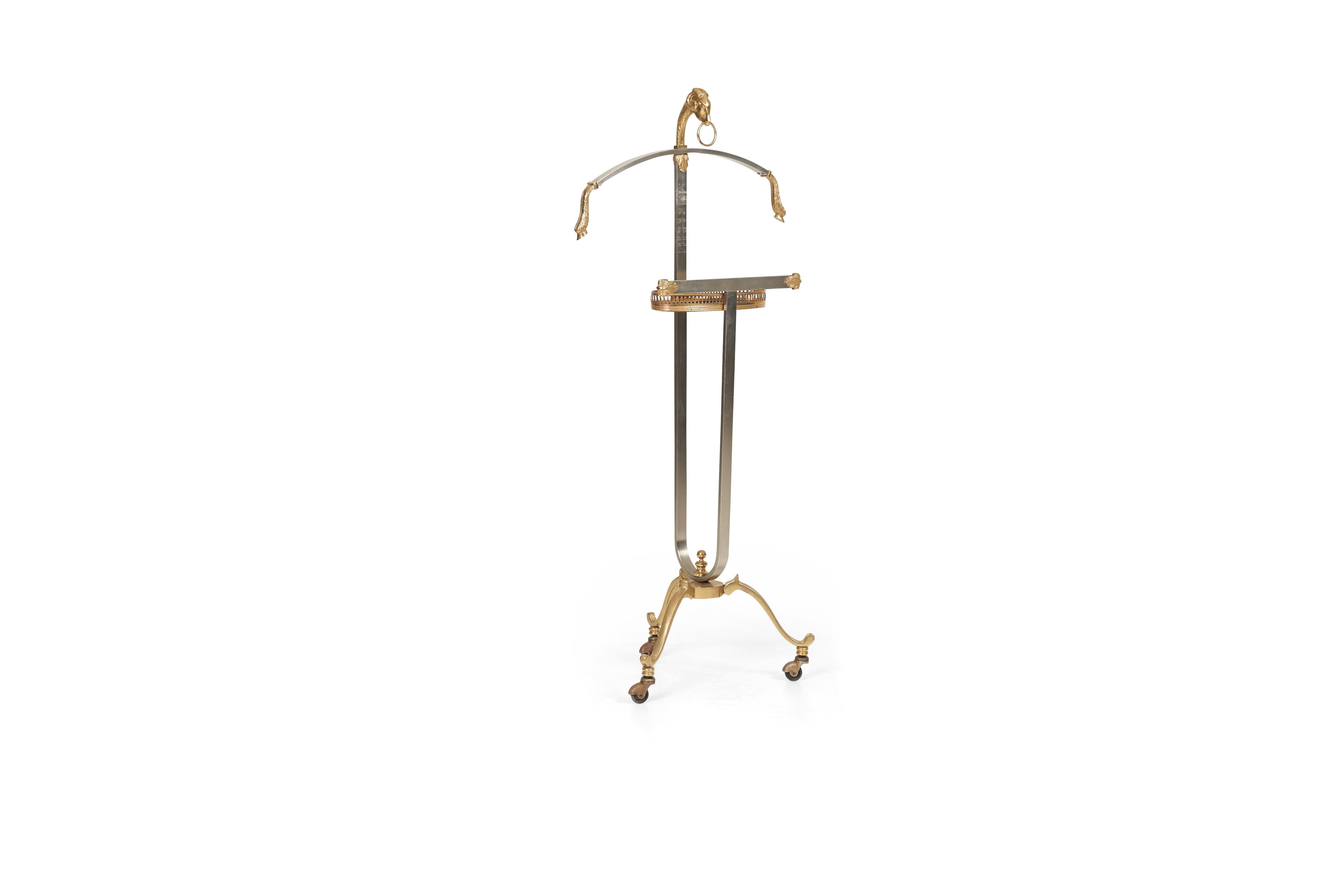 Maison Jansen (French, founded 1880) Ram's head valet, circa 1960. Italian, brass and brushed stainless steel, curved jacket bar with brass hooves, adjustable stem, galley rail tray, terminating on tripod base with casters.
(Stamped made in Italy).