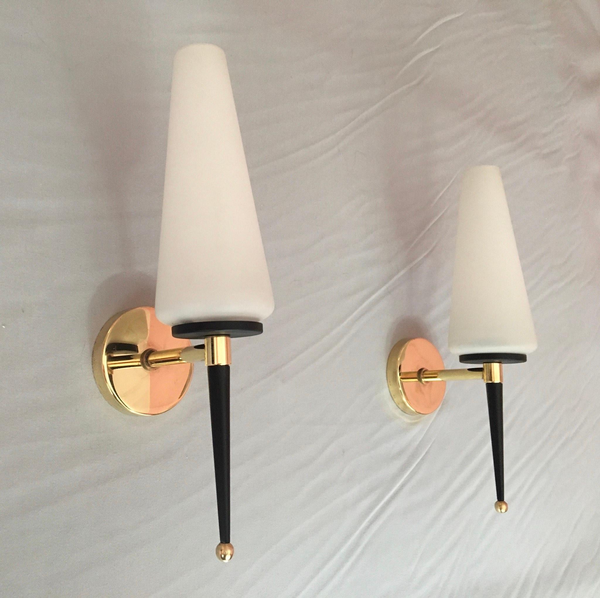 Very elegant pair of French single sconces wall lights of the mid 1950's by Maison Lunel in brass, black painted metal and white satin Opaline glasses shades. The pair is in a really very good condition, electrical parts have been renewed and fit