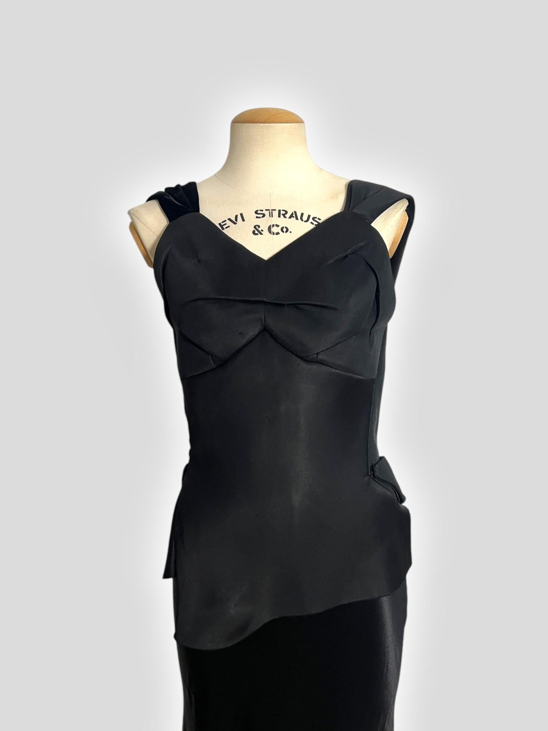 Este impresionante vestido de Maison Margiela by John Galliano Otoño 2015 encarna la elegancia dramática y la precisión arquitectónica. El corpiño estructurado presenta esculturales tirantes de terciopelo negro y un estrecho peplum asimétrico en la