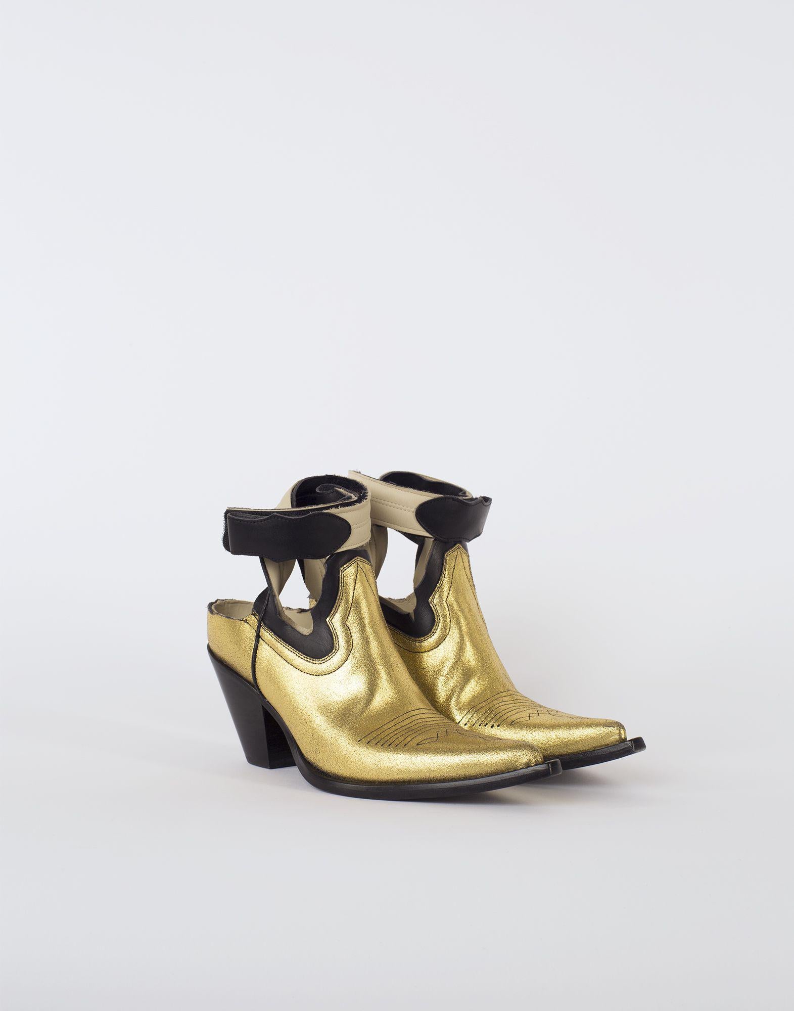 Metallic-goldene Cowboy-Stiefel mit Cut-Out, gezeigt auf dem Maison Margiela Frühjahr-Sommer 2018 Laufsteg für Damenmode. Die klassischen Cowboystiefel wurden durch die Décortiqué-Technik auf die wesentlichen Elemente reduziert. Diese Stiefel sind