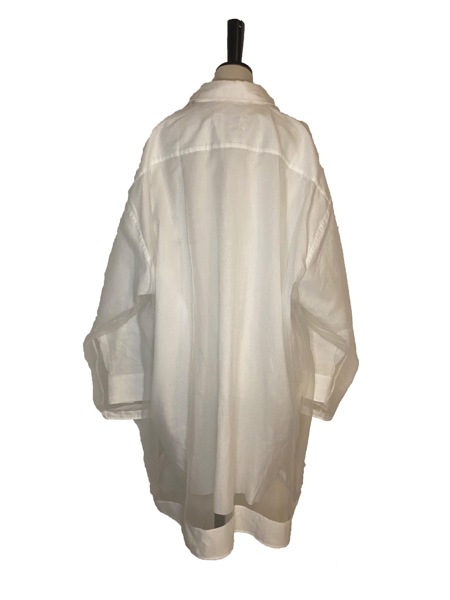 Abito camicia a maniche lunghe in cotone bianco in stile classico di Maison Margiela. Vestibilità oversize con chiusura frontale a bottoni. Colletto classico, tasca sul petto e polsini con bottoni. Lunghezza al ginocchio. Il rivestimento in tulle