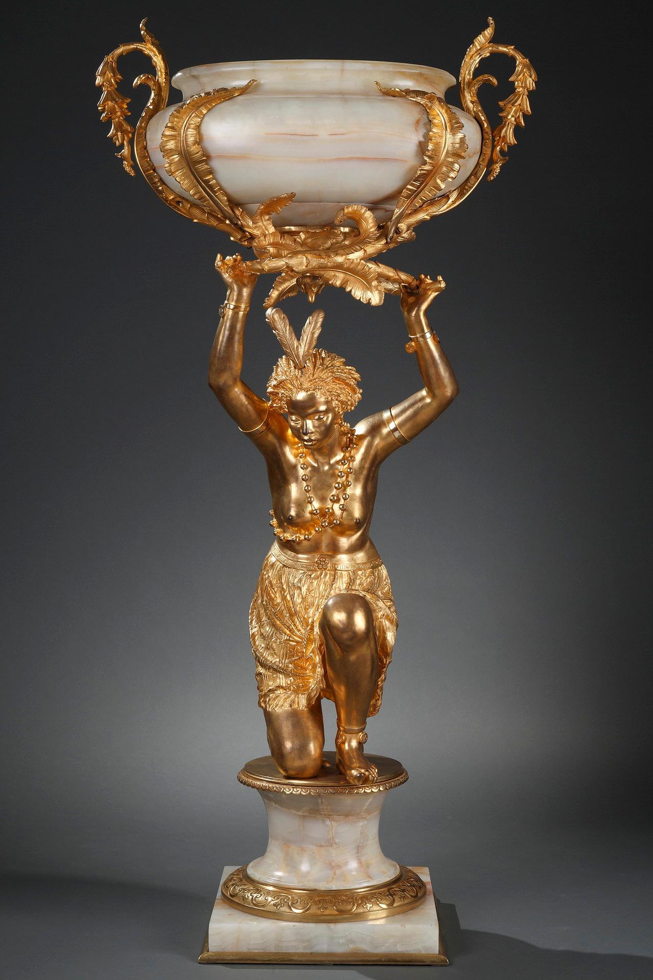 Eccezionale fioriera della Maison Marnyhac in bronzo cesellato e dorato e onice algerino che rappresenta una giovane donna africana inginocchiata che porta una ciotola ovale decorata con fogliame. È vestita con un perizoma, indossa una garzetta ed è