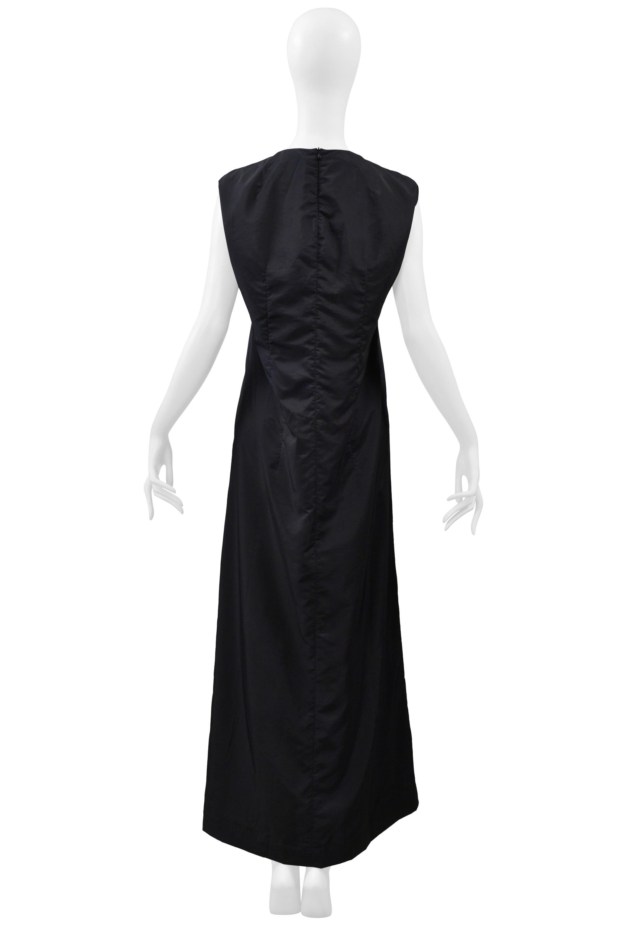Resurrection Vintage est heureux de vous proposer une robe classique noire minimale de Maison Martin Martin, avec des emmanchures circulaires emblématiques et un corps long et étroit avec une légère forme A-line. L'imperméable assorti est vendu