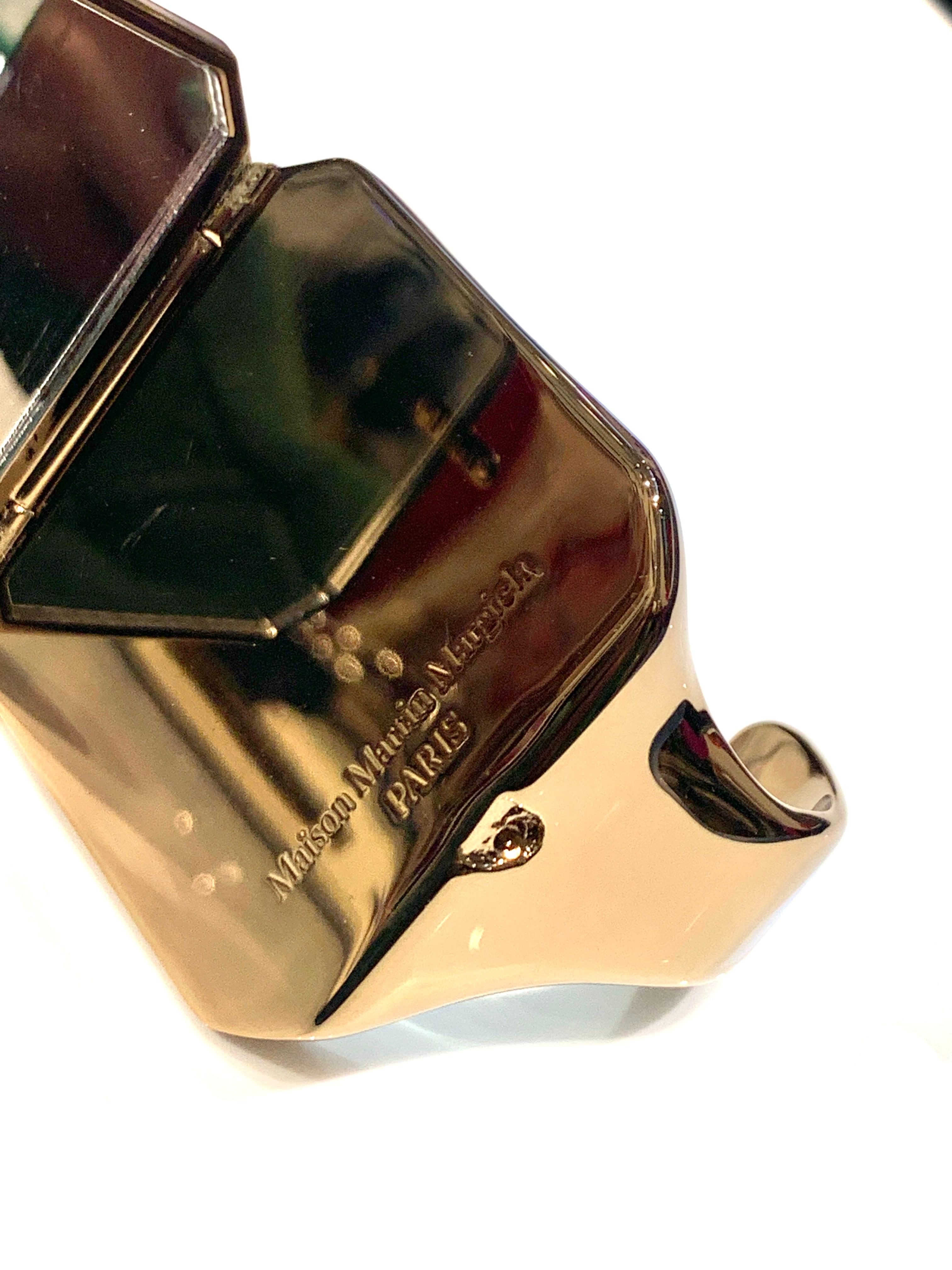 Gioiello-Brace mit Spekulatius aus der eigenen Kollektion von Maison Martin Margiela. 
Il materiale del gioiello è ottone lucido e riflettente di colore oro scuro.
Der Bügel wird durch einen immer leuchtenden Kern nach vorne geschoben und durch