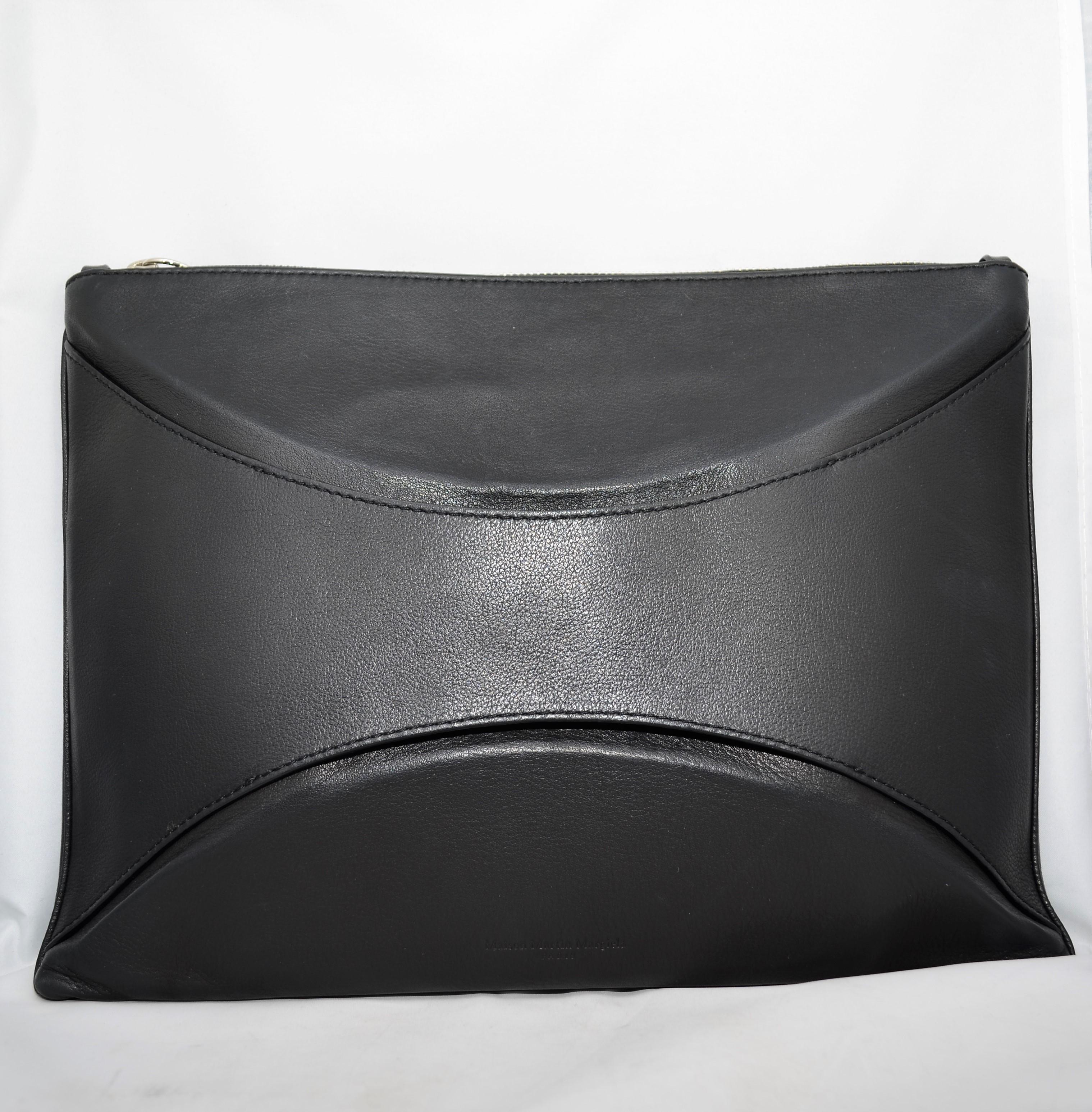 Maison Martin Margiela Clutch featured in black calf leather with silver-tone hardware throughout, a top zipper closure, and suede lining. Clutch has an optional shoulder strap or can be held by the outer leather detail as pictured. Made in