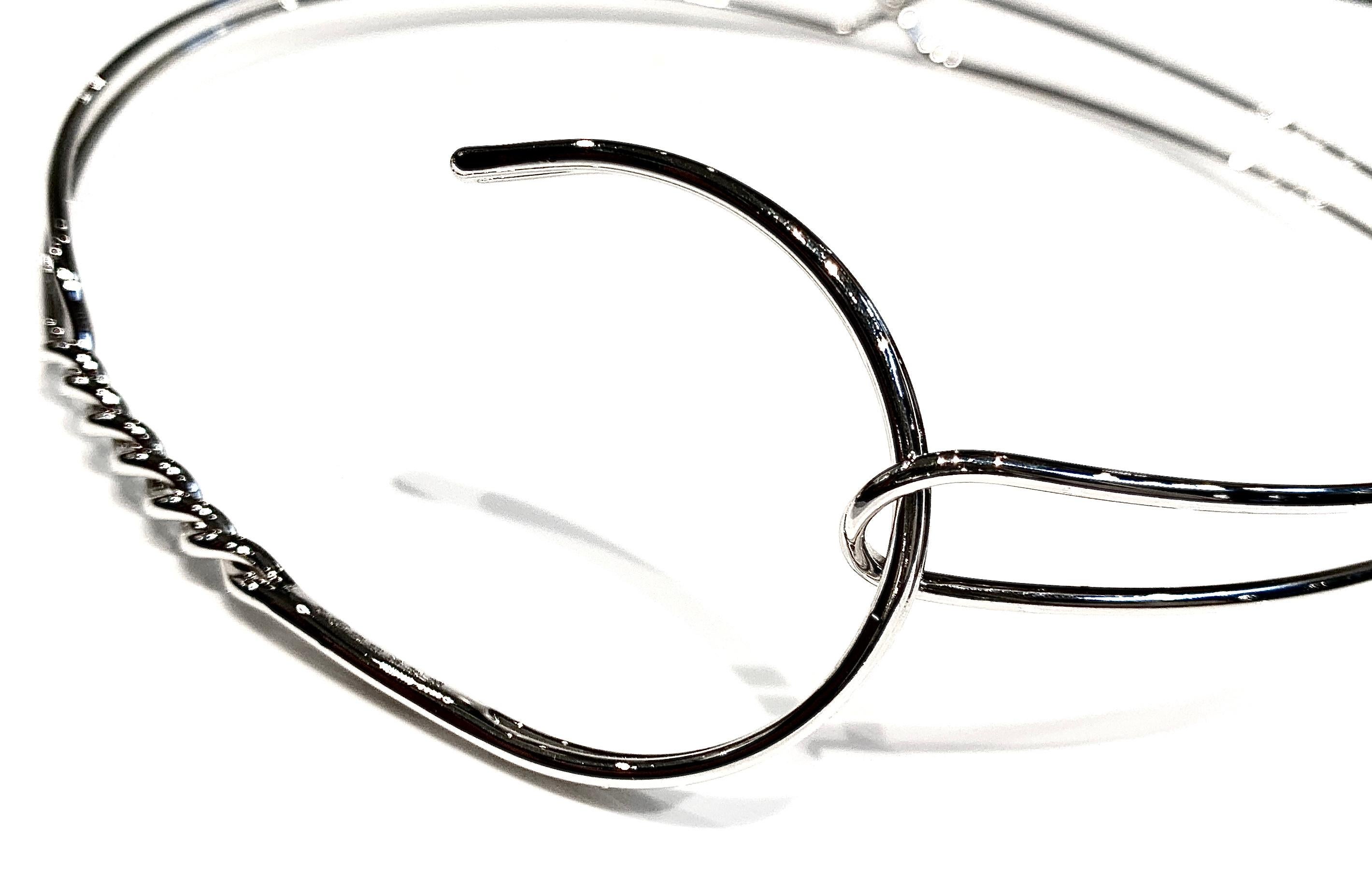 Collana dei primi anni 2000 di MAISON MARTIN MARGIELA circolare a forma di appendi abiti, in filo è metallico e lucido, color argento. 
Se compone de un doble filo que se encuentra simétricamente en el centro, para luego dividirse y terminar en el