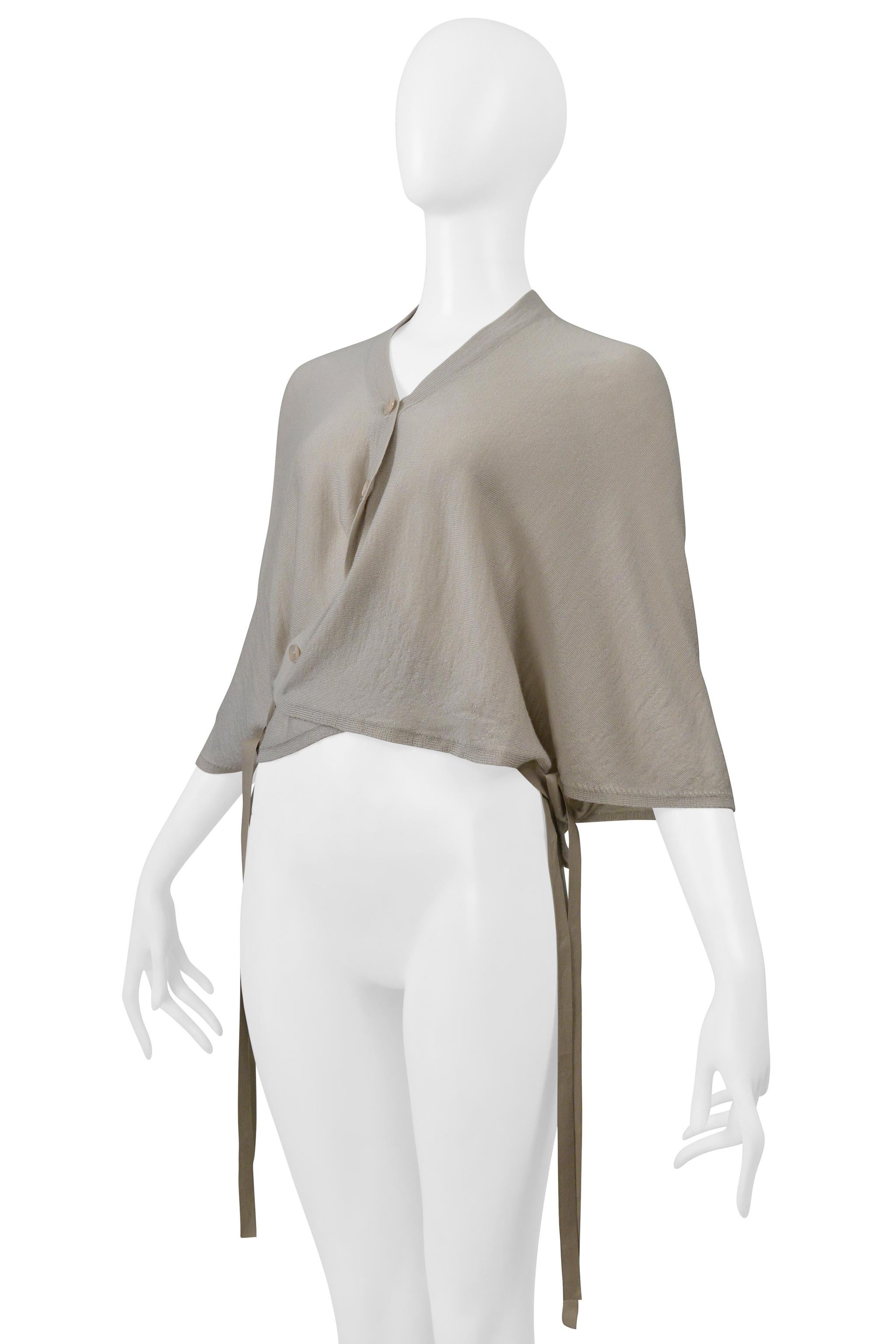 Resurrection Vintage freut sich, eine graue Strickjacke von Maison Martin Margiela aus der Frühjahrskollektion 2000 präsentieren zu können. Sie hat Knöpfe an der Vorderseite, Dolman-Ärmel, ein Wickel-Design und angebrachte Bänder.

Maison Martin