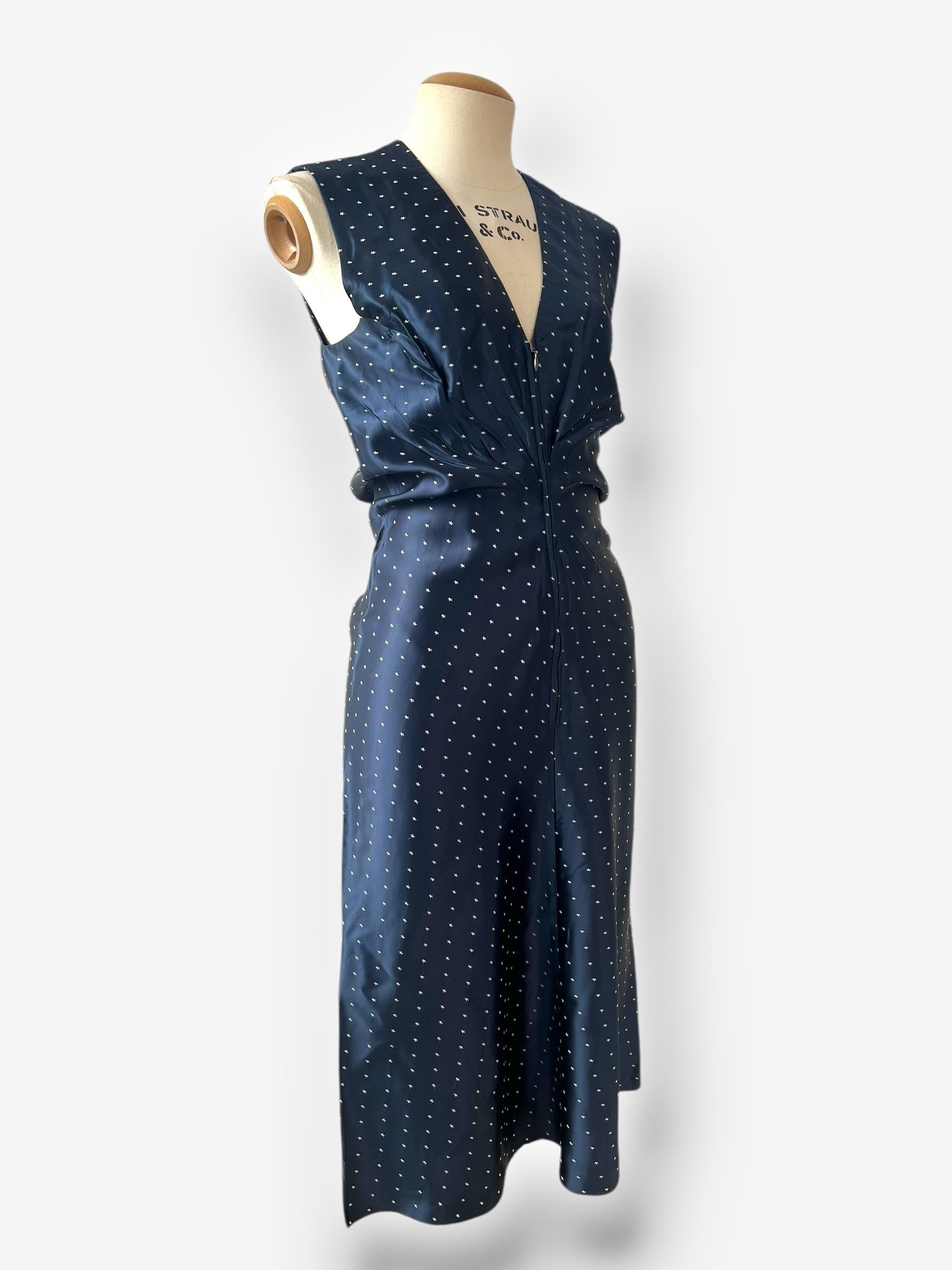 
From Margiela’s Spring/Summer 2007 collection, this navy sleeveless dress features a delicate scattered star print on a fluid silk-blend fabric. The front is softly gathered and draped at the waist with a subtle V-neckline and zip fastening. The
