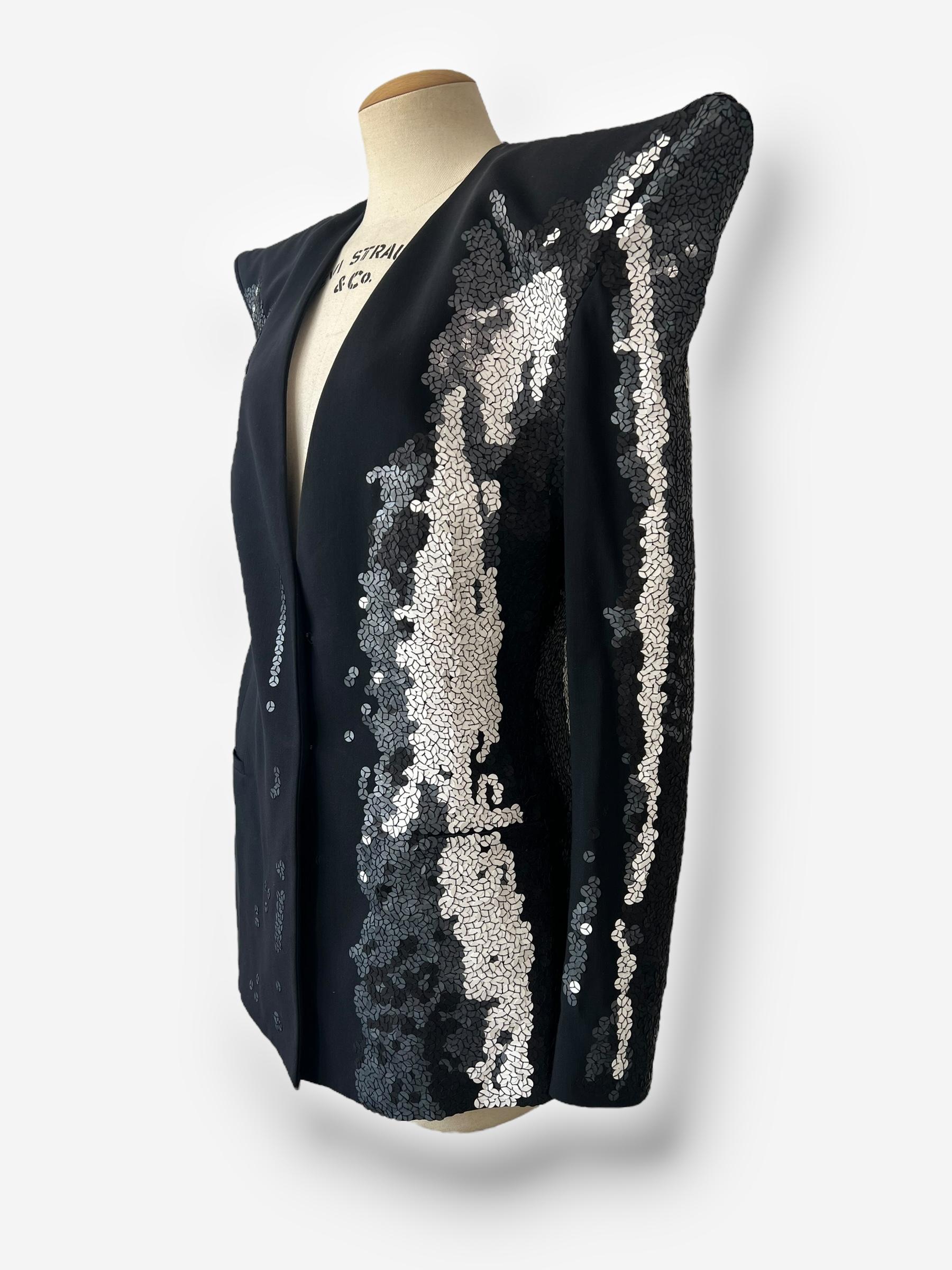 Llama la atención con este llamativo blazer de la colección Primavera/Verano 2008 de Maison Martin Margiela. Presentado en el número 33 de la pasarela, tiene unos hombros esculturales y un motivo abstracto de lentejuelas plateadas y negras que capta
