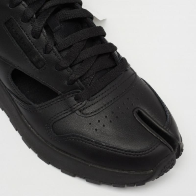 A gladiator-style sneaker from Maison Martin Margiela's collaboration with Reebok! These Tabi high-top sneakers are in black leather, featuring the famous 'Tabi' toe and cuts for an open look. The laces, velcro strap, and rubber soles give the