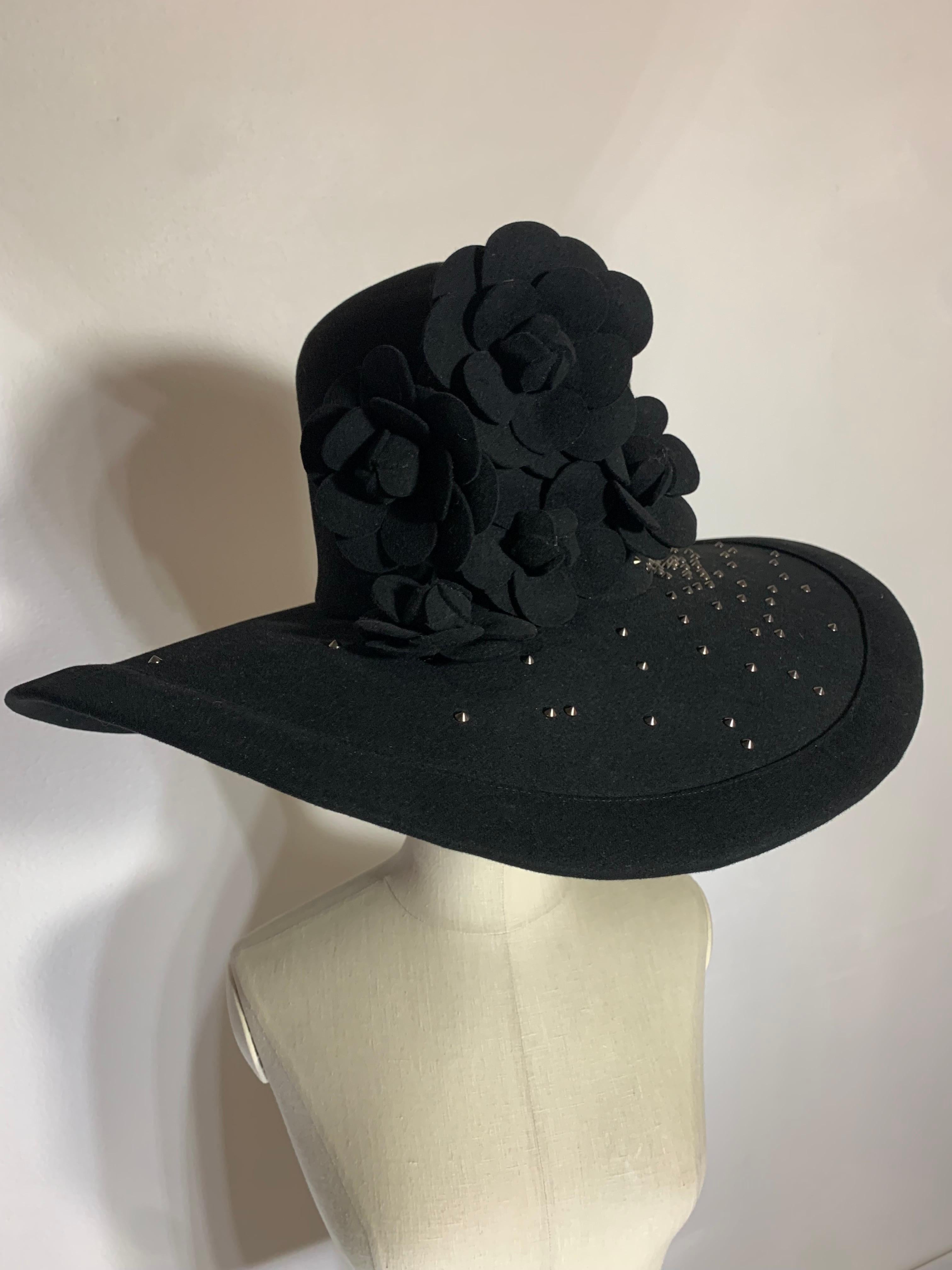 Maison Michel Black Large Brimmed Felt High Crown Hat w Studs & Camellia Flowers: Silver triangular metal stud embellishments are found scattered on brim body and crown. Large bouquet of cascading black felt camellia at front of hat. Brim falls in a