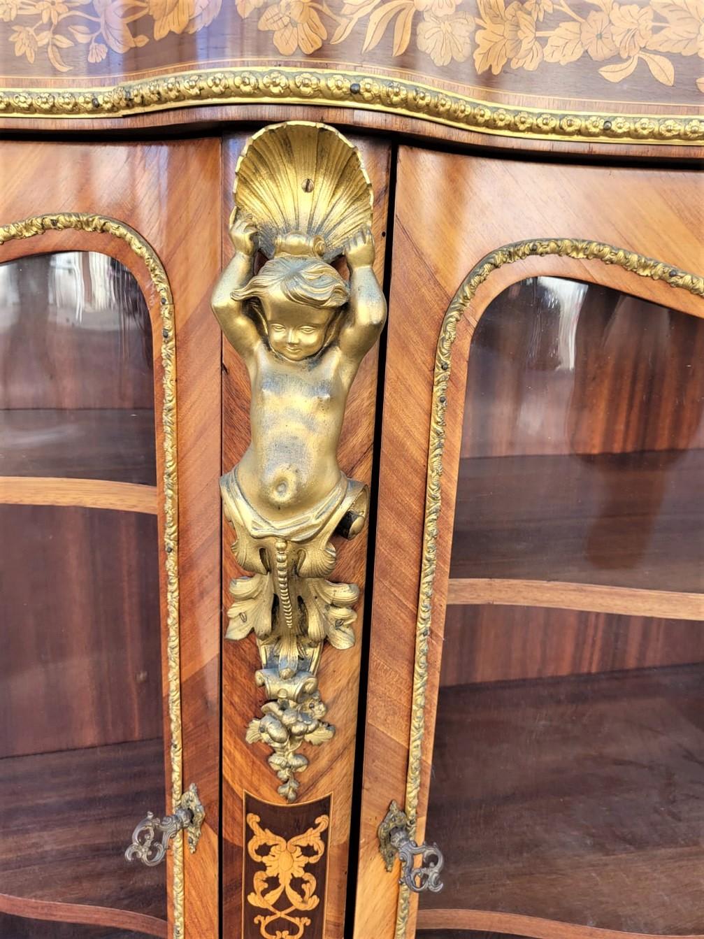 Very beautiful sideboard t in marquetry with gilded bronze ornamentations: the upper part is decorated with a frieze with floral motifs, the 3 curved and glazed doors are separated by putti each bearing a shell, the base is decorated with bronzes