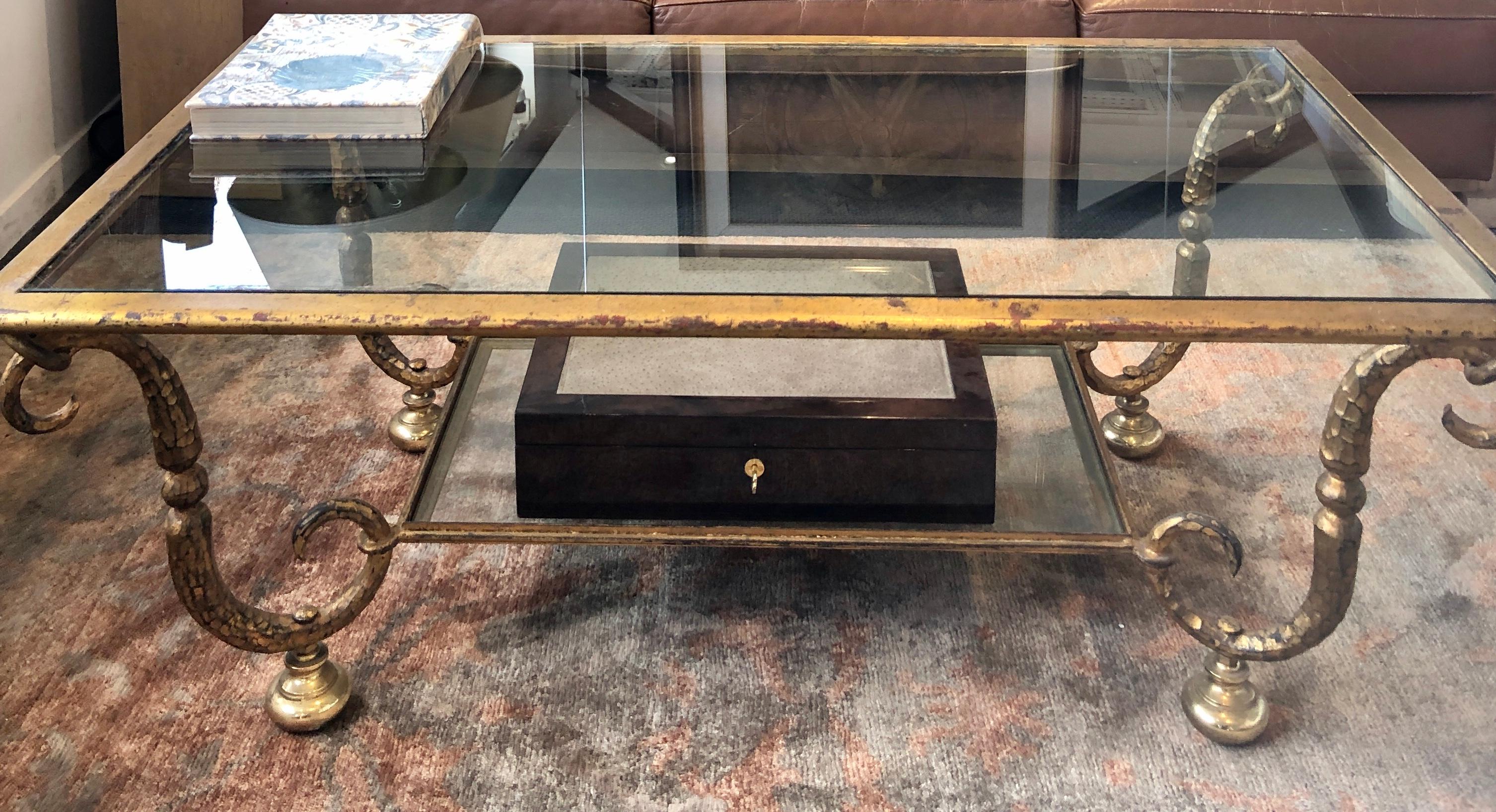 Rectangular coffee double tray coffee table from the French Maison Ramsey with hammered forged iron structure, scroll-shaped legs patinated with gold leaf finishing,
The top glass is thick and the end of the legs are placed on a solid brass