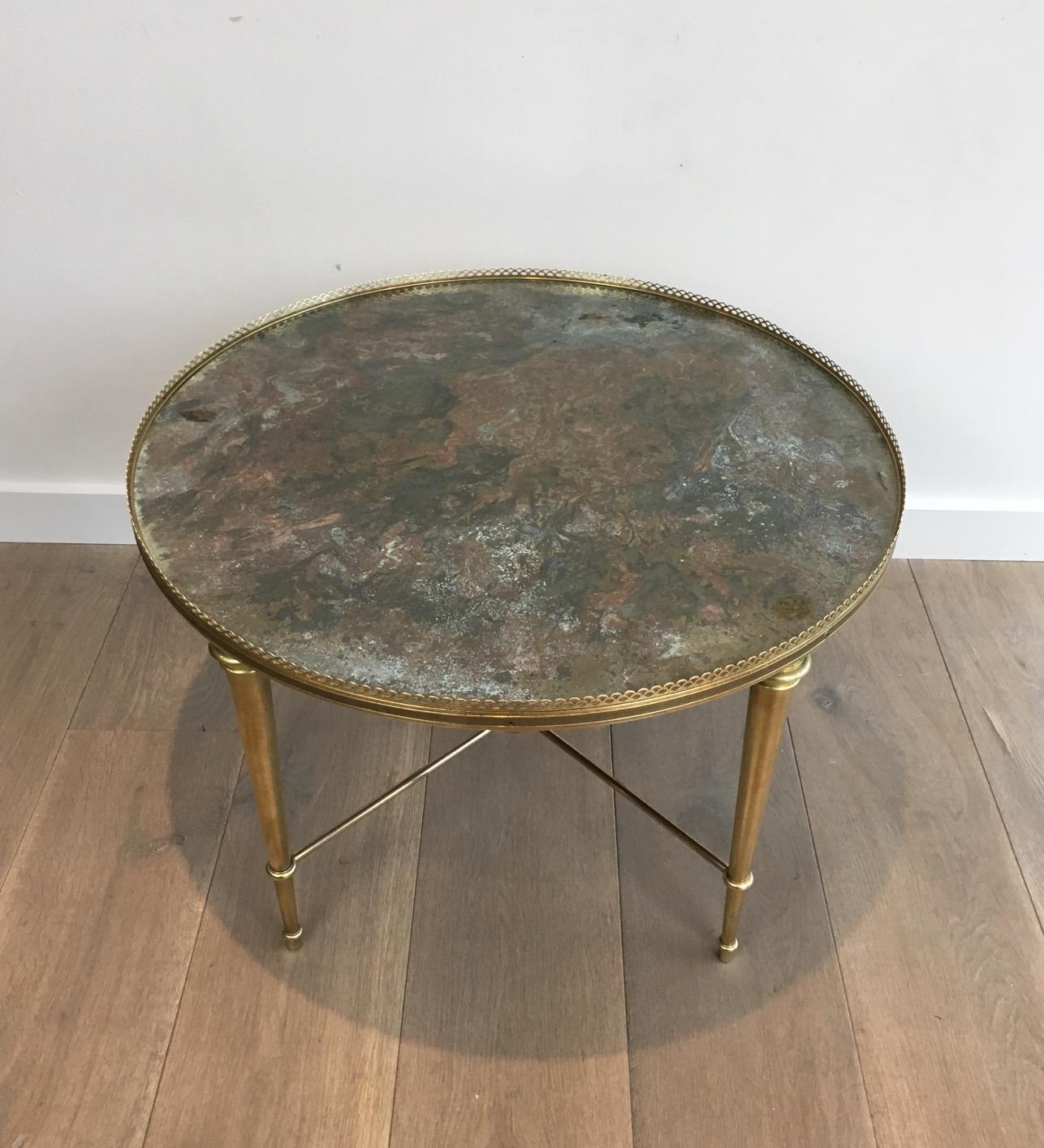 This neoclassical round coffee table is made of elegant brass feet joigned by a stretcher on which centre is a nice finial. The top is made of a beautiful verre églomisé surrounded by a fine brass gallery. This cocktail table was made by French