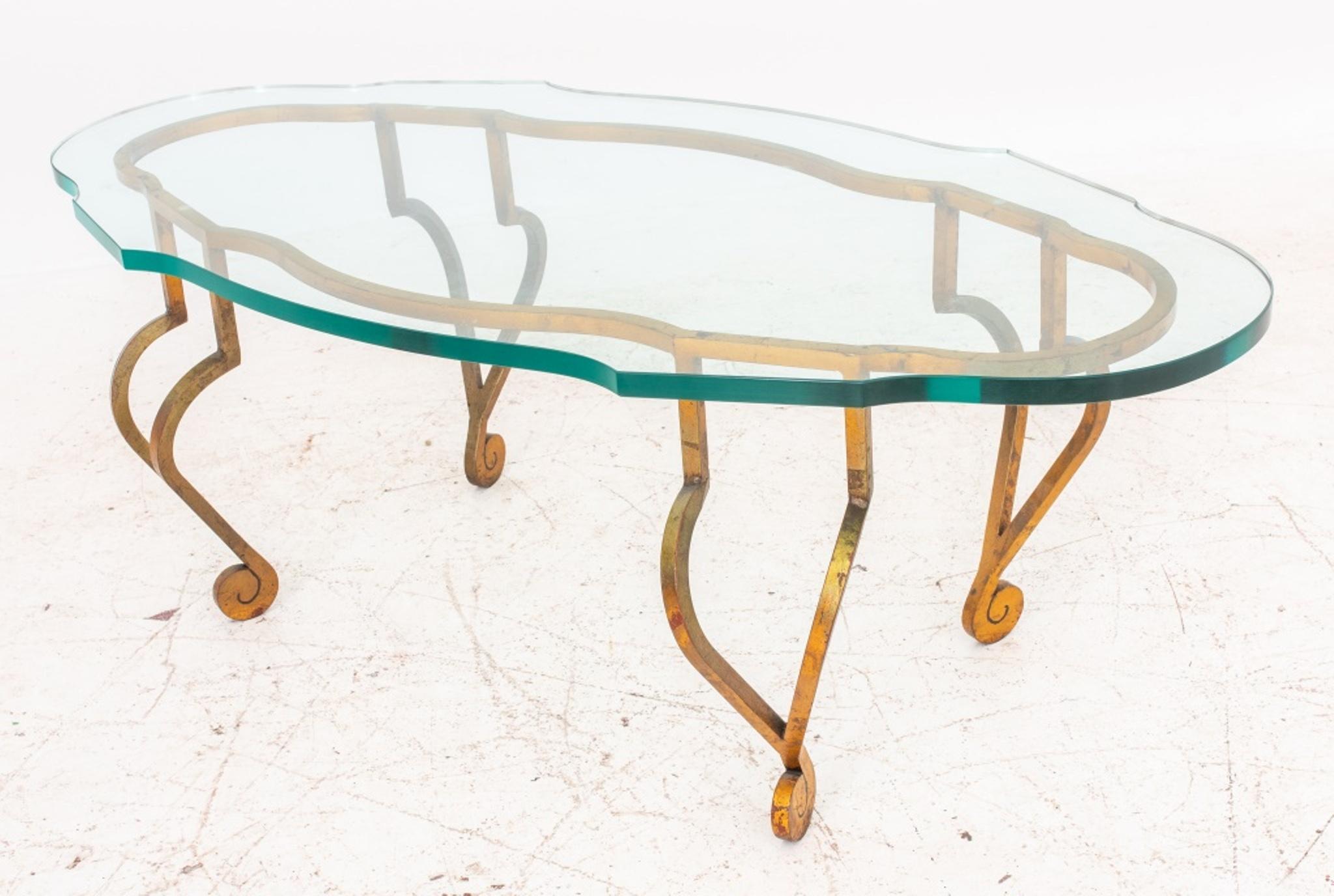 Hollywood Regency gilded wrought iron low coffee or cocktail table, 1950s, after the model by Jean Charles Moreux (French, 1889 - 1956) for Maison Ramsay, with shaped oval top above conforming lacquer-gilded wrought iron base with curving legs in