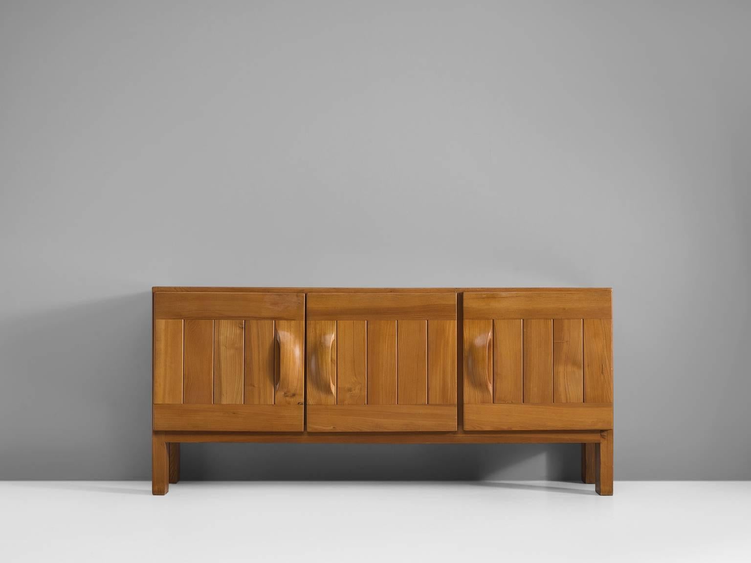 Credenza by Maison Regain, elm, France, 1960s.

This exquisite credenza combines a simplified yet complex design combined with nifty, solid construction details that characterize Maison Regain's designs. The three well balanced, sturdy doors are