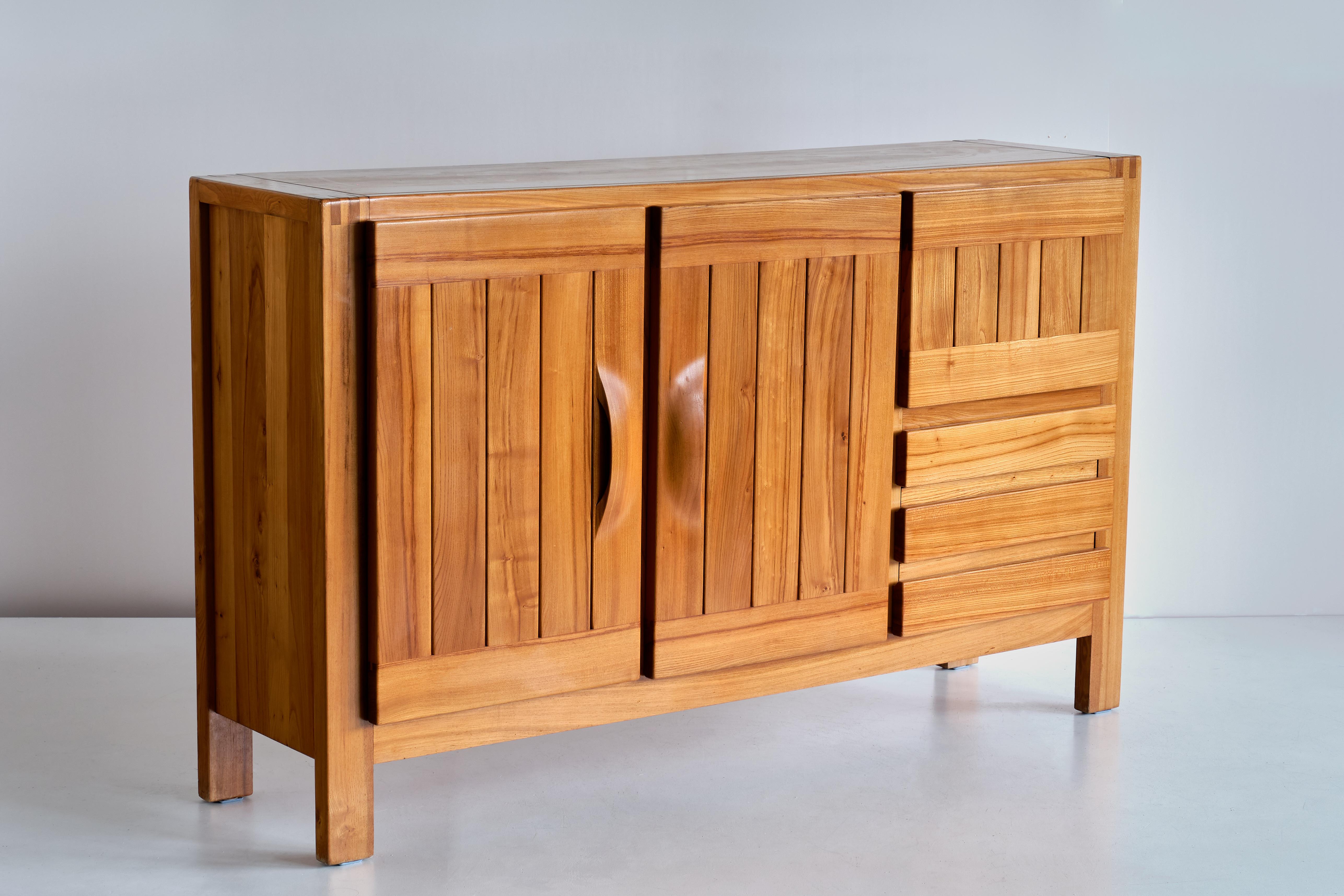 This impressive high sideboard was produced by Maison Regain in France in the late 1970s. The sideboard is made in solid elmwood and has a double door on the left with two beautifully crafted, sculptural handles. A convenient flap style opening and