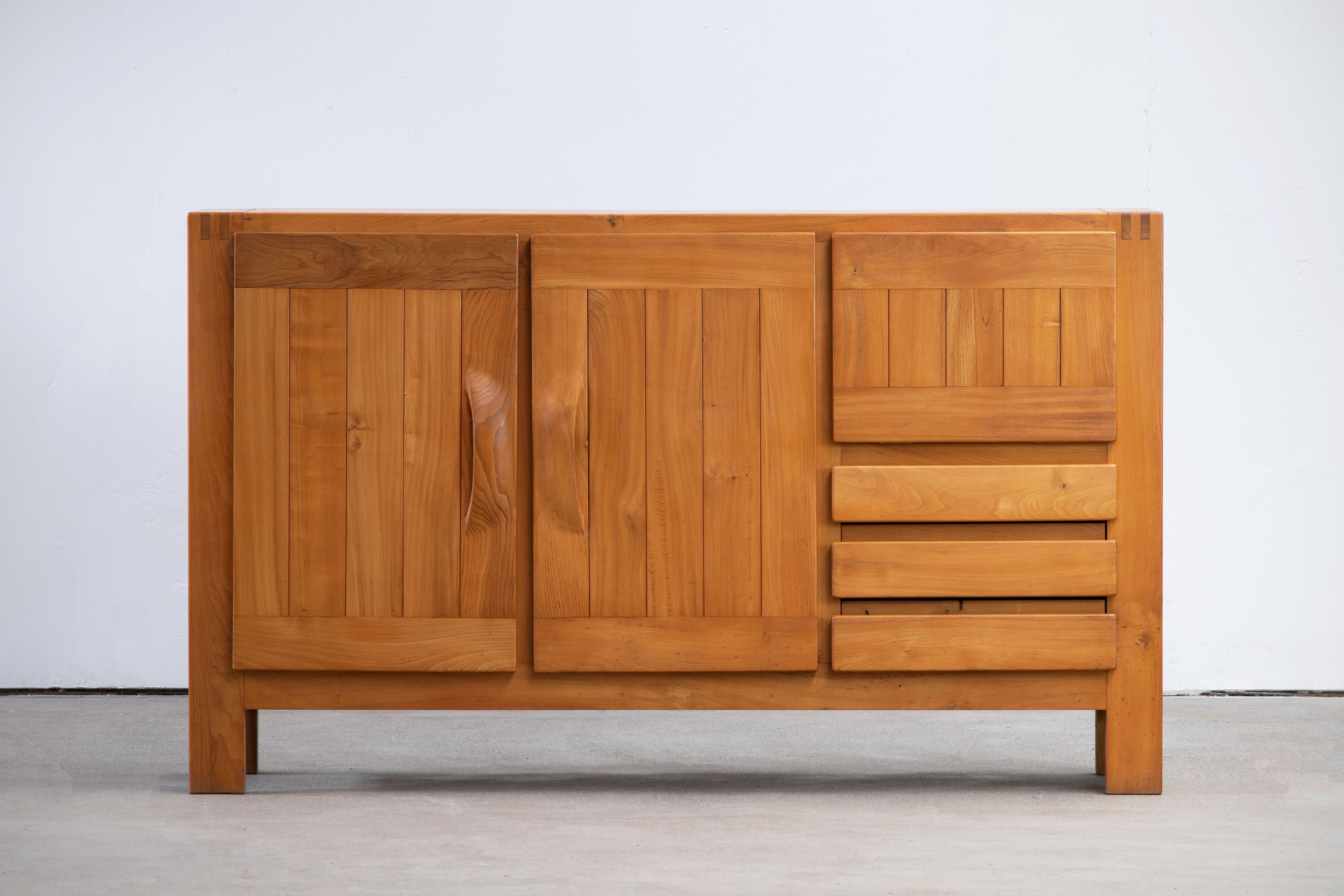 This impressive high sideboard was produced by Maison Regain in France in the late 1970s. The sideboard is made in solid elmwood and has a double door on the left with two beautifully crafted, sculptural handles. A convenient flap style opening and