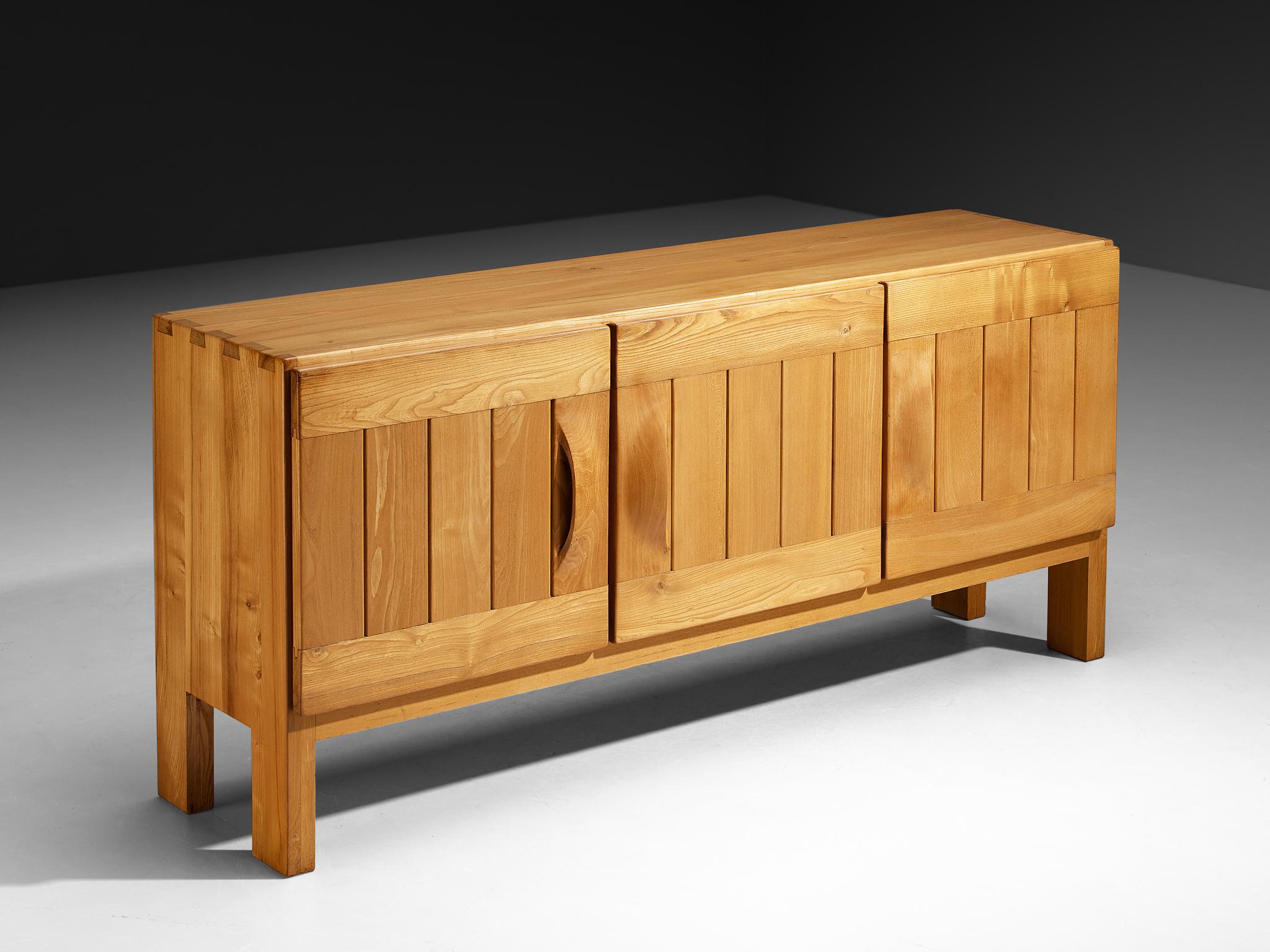 Maison Regain, credenza, olmo, Francia, anni '60.

Questa credenza di Maison Regain combina un design semplificato ma complesso con dettagli di costruzione solidi e ingegnosi che ne caratterizzano il design. Le tre porte, equilibrate e robuste, sono