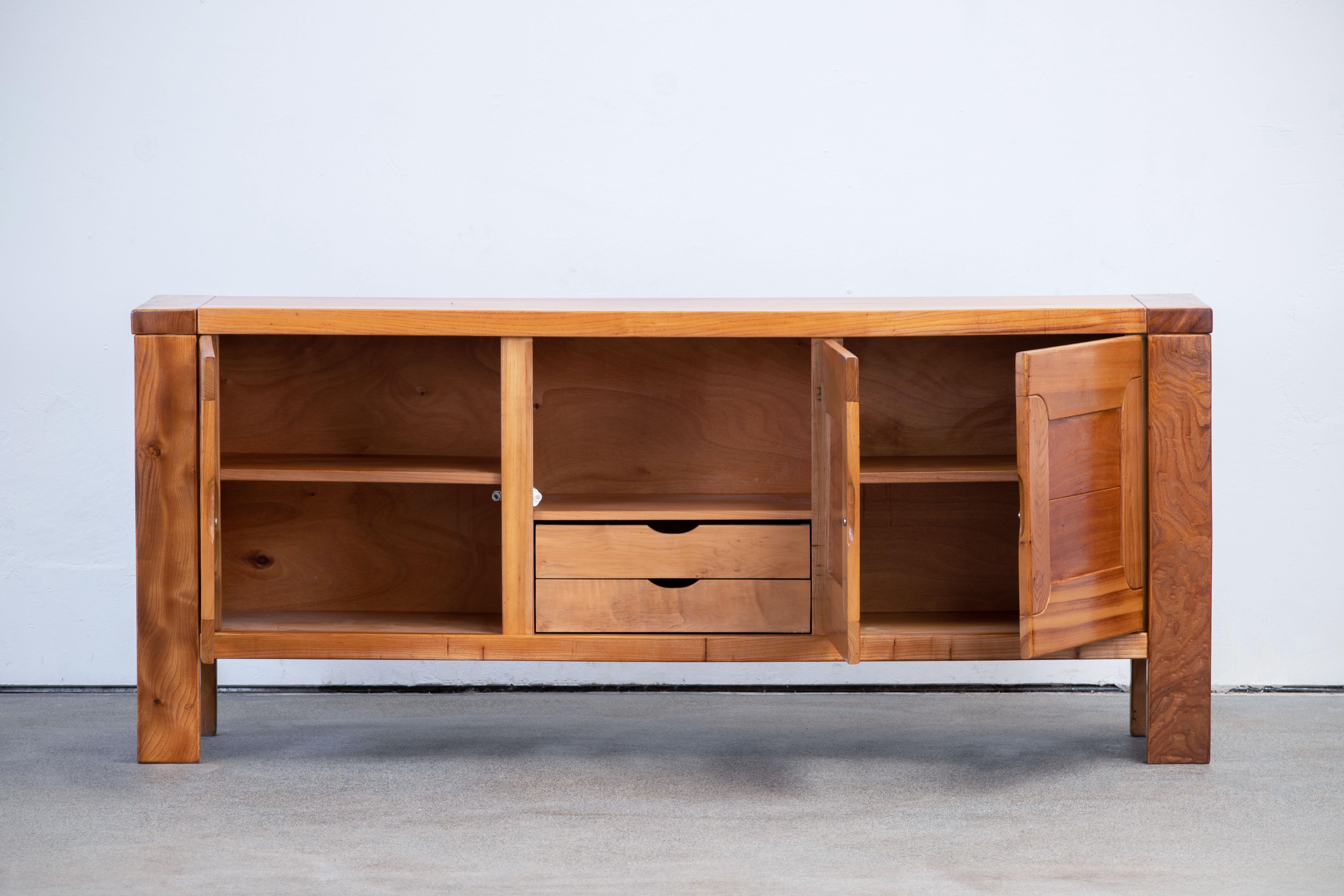 This impressive sideboard is attributed at Maison Regain, France in the late 1970s. The sideboard is made in solid elmwood and has a double door on the left with two beautifully crafted, sculptural handles. 
The wooden connections on the top, the