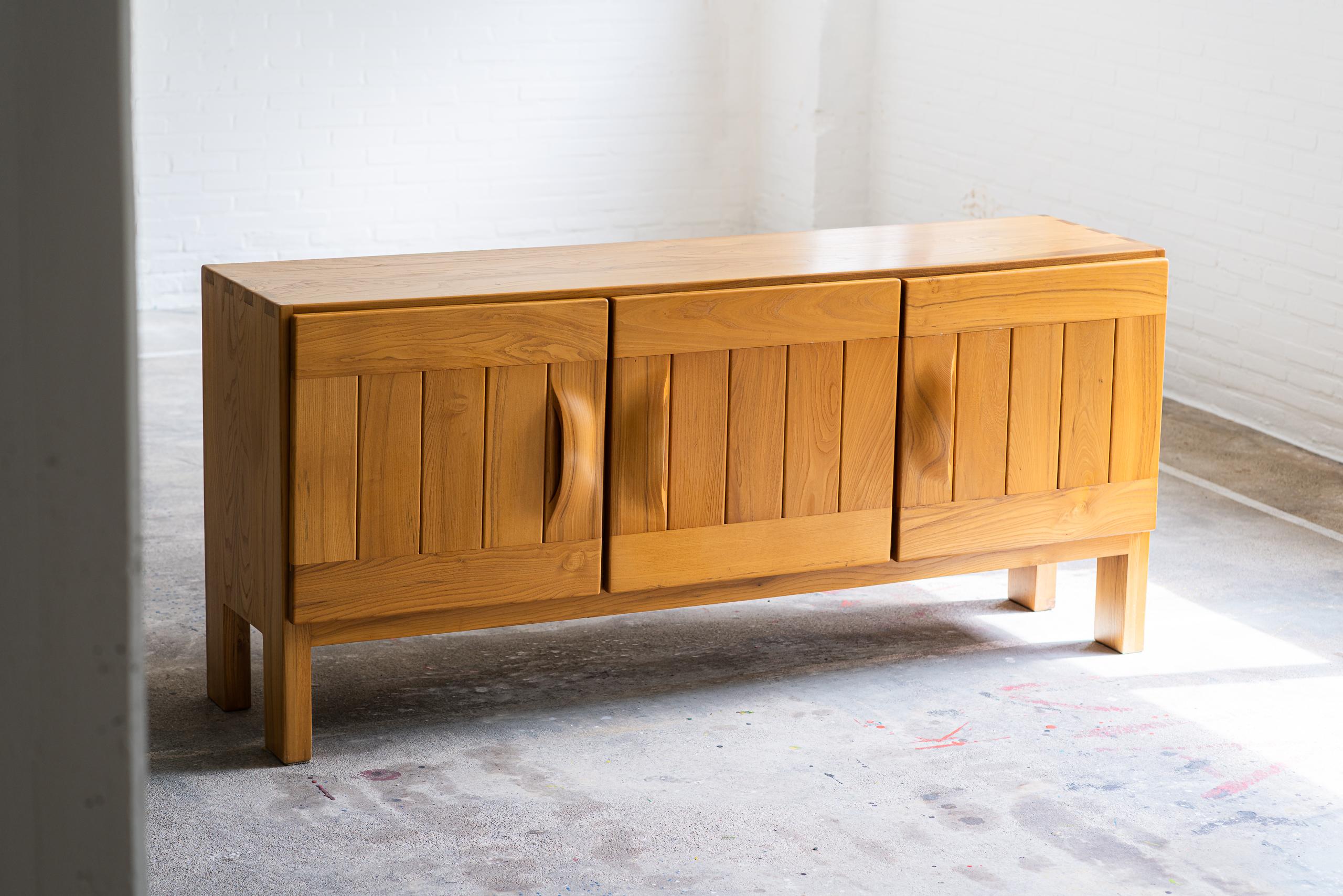 French sideboard produced by Maison Regain in solid elm wood. The finger joints on both upper corners and the large solid wood door pulls are very typical for Maison Regains designs and craftsmanship. The heavily made doors give you access to a