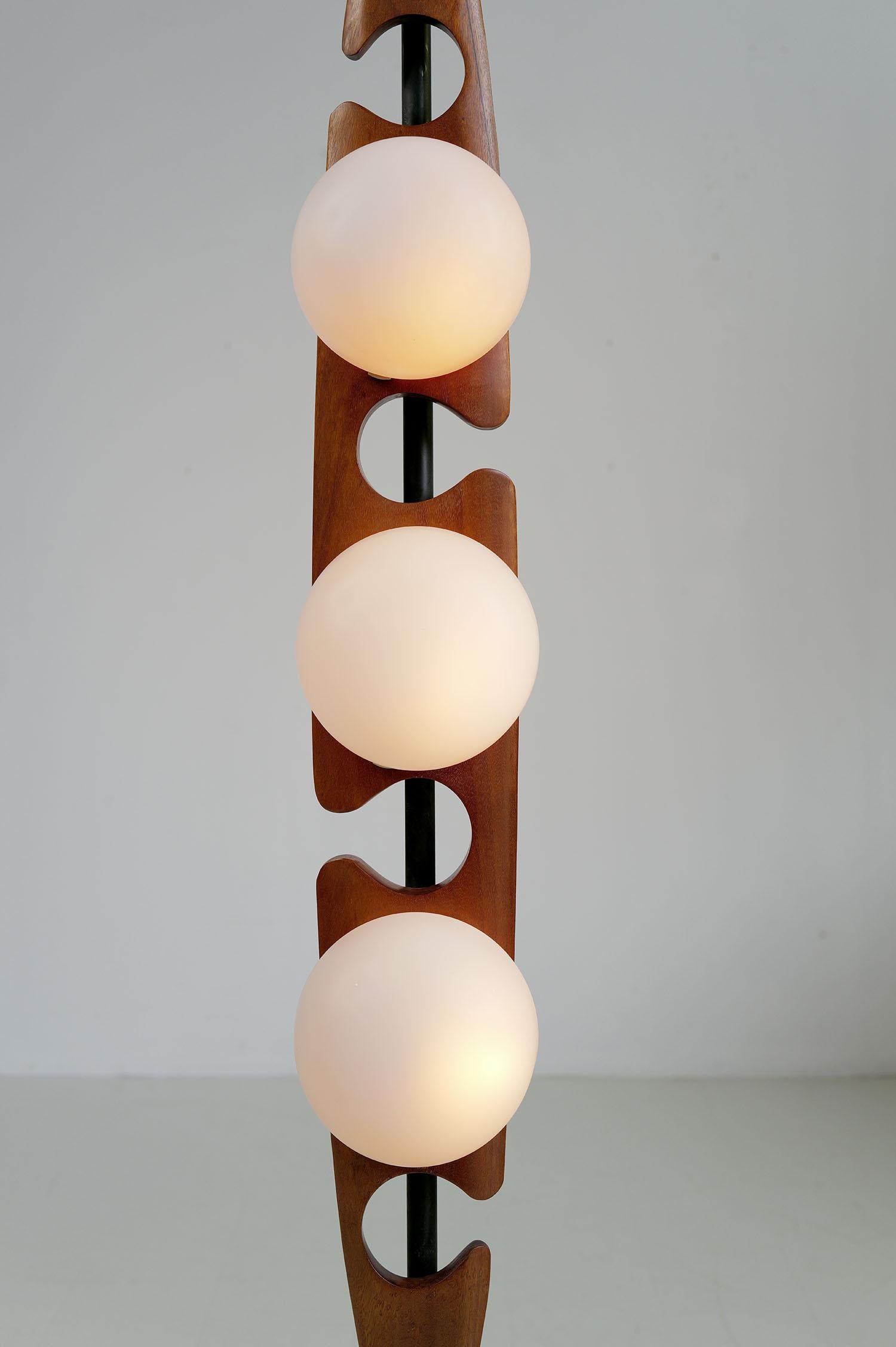Lampadaire en teck et métal par Maison Rispal, France 1960. Une tige centrale tubulaire repose sur une base en métal noirci. Les trois réflecteurs en verre dépoli sont fixés sur une pièce évidée en bois de teck massif. Ce luminaire est l'une des