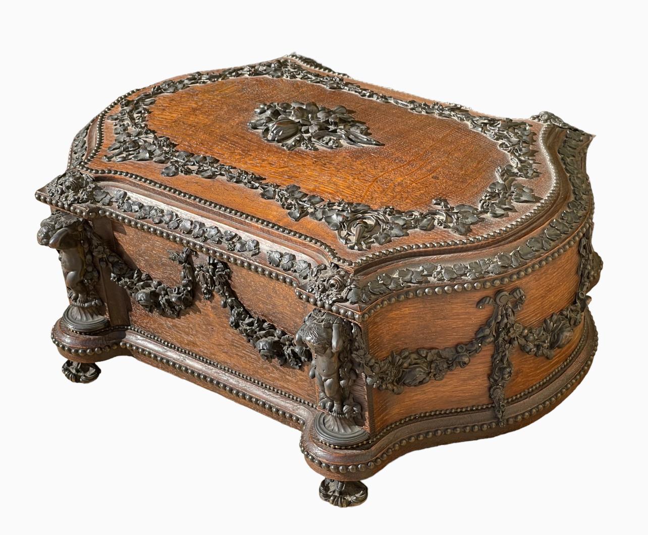 Large oak box carved on all sides richly decorated with garlands of flowers and bronze foliage. 4 bronze puttis adorn the 4 corners of this box. Signed on the lock 