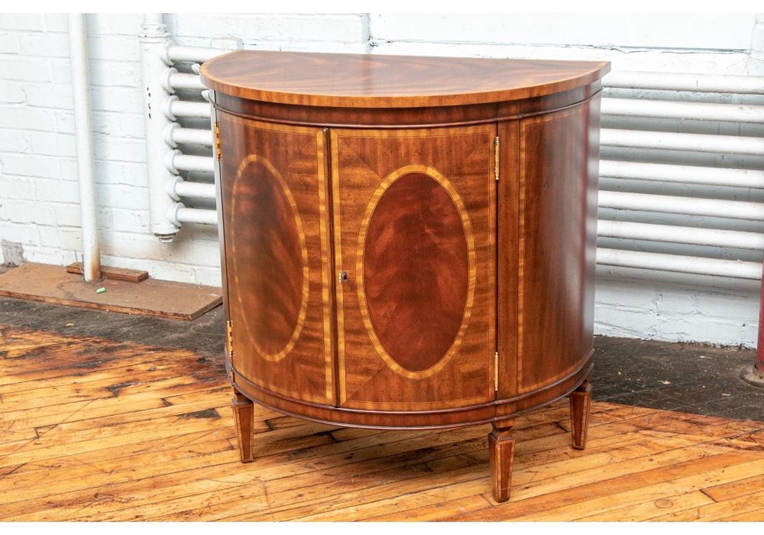 Handsome mahogany cabinet with banded top, side panels and doors. Striking flame mahogany veneers.
Tapered legs and curved 2 door front with brass key and hinges. Left hand door has top and bottom side locks.
Interior has an adjustable