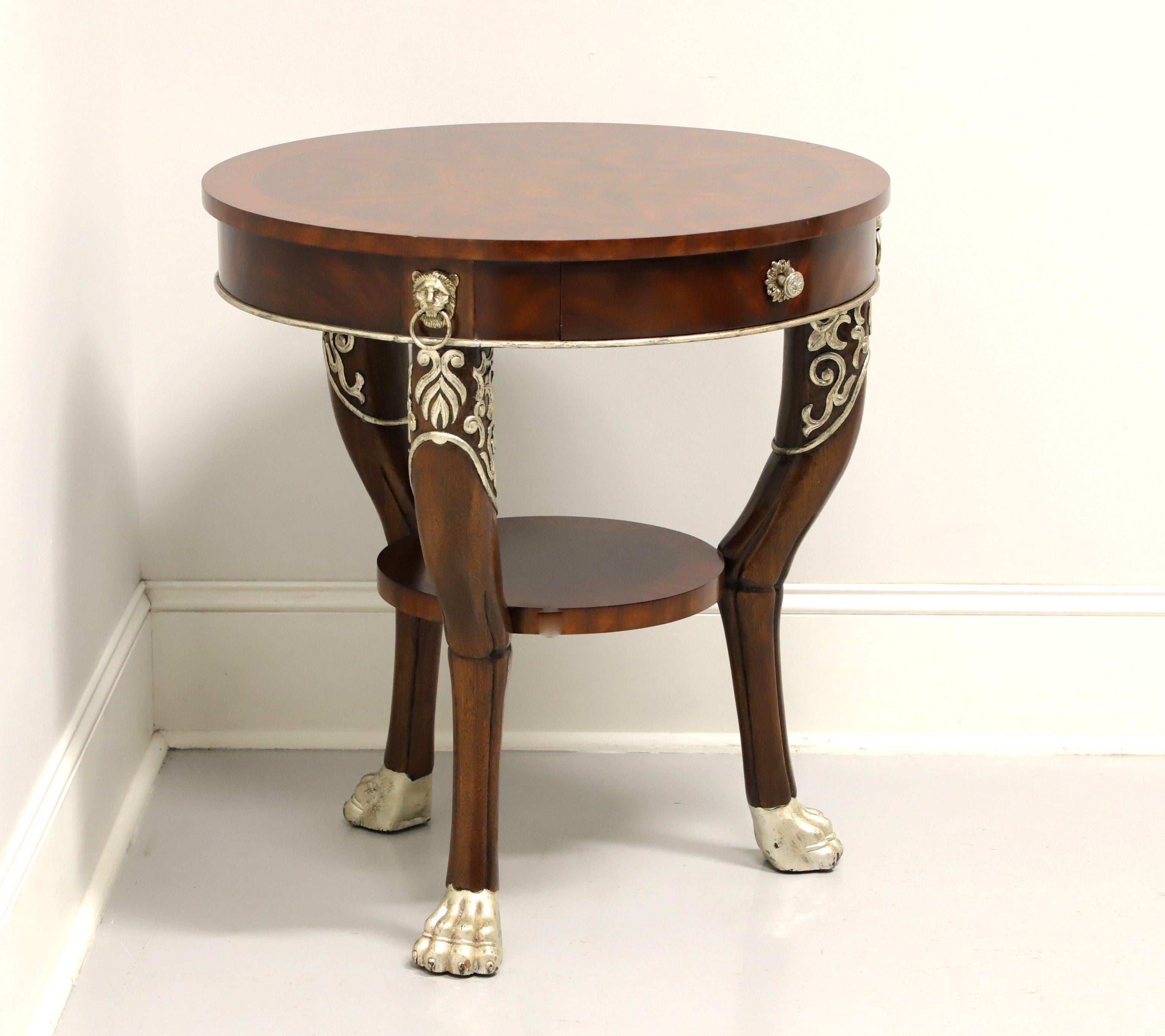 A round accent table in the Regency style by Maitland Smith. Mahogany with banded & inlaid flame mahogany top, decorative metal hardware including three lion masks holding a ring over the legs, silver-gold color painted carved accents to apron &