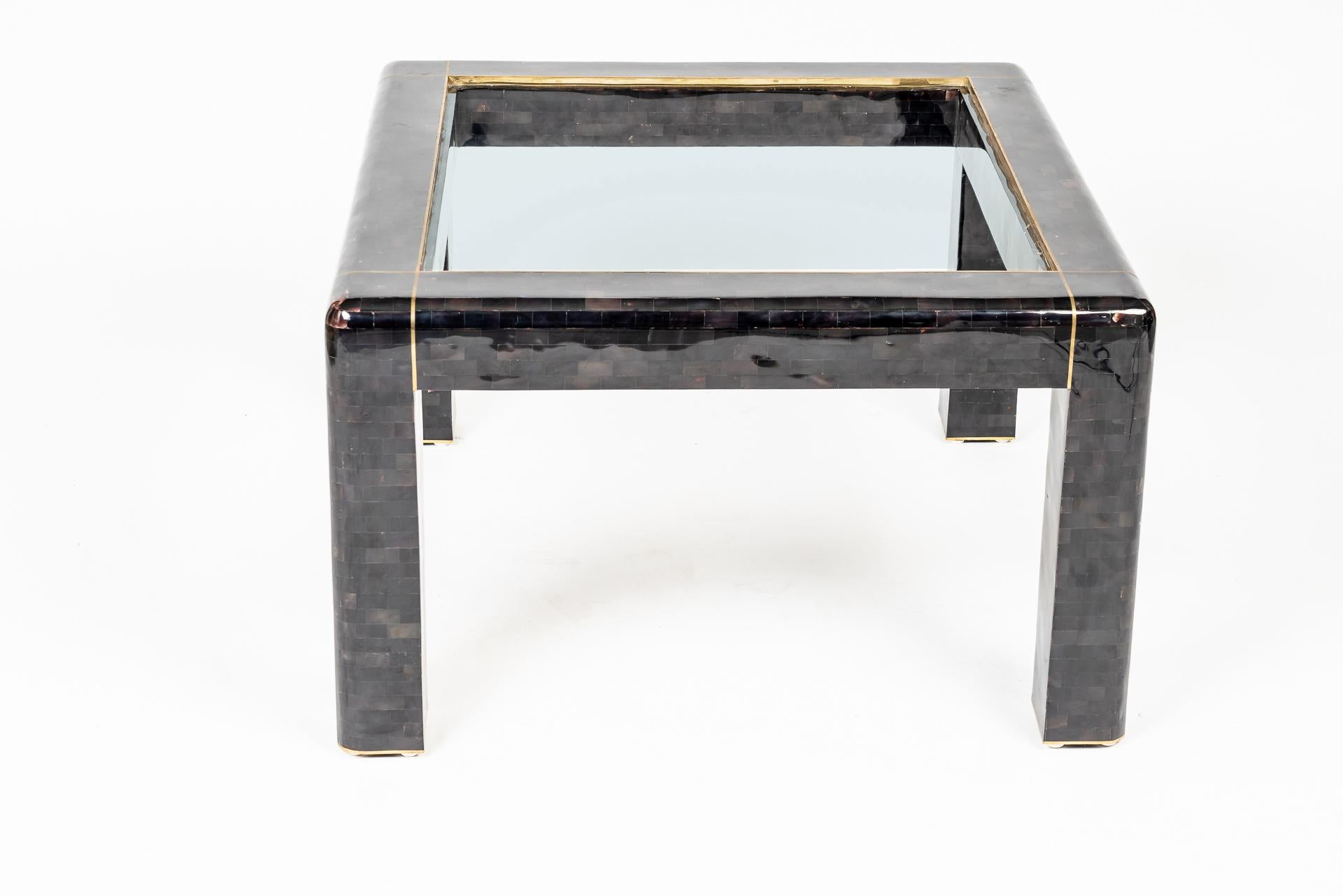 This beautiful manufactured side table by Maitland Smith shows the delicate work with materials like shell mosaic. The structure is covered by rectangular dark colored shell mosaic pieces and has at the top a small brass inlay as well as a glas