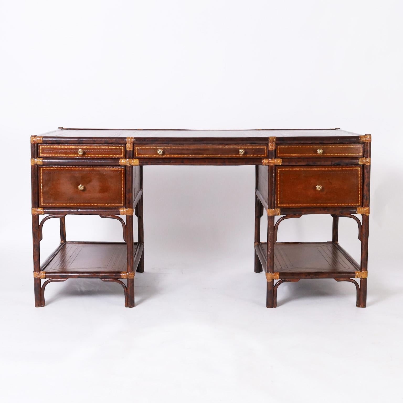 Handsome midcentury British Colonial style desk having a tooled and gilt decorated brown leather top, a five drawer case with tooled leather all around, brass hardware, and two leather lined lower tiers.