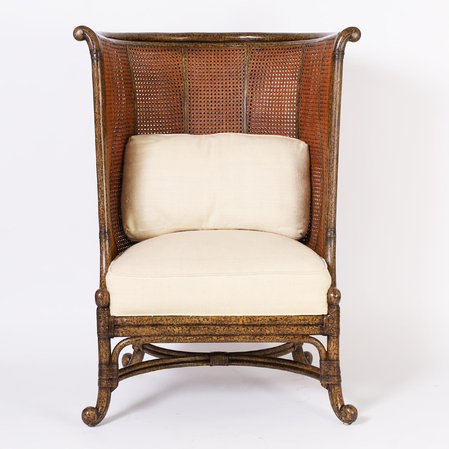 Standout vintage stylized tropical wingback chair with a faux tortoise frame crafted in hardwood, double caned sides and back, upholstered seat, reed wrapped joints and rolled feet.