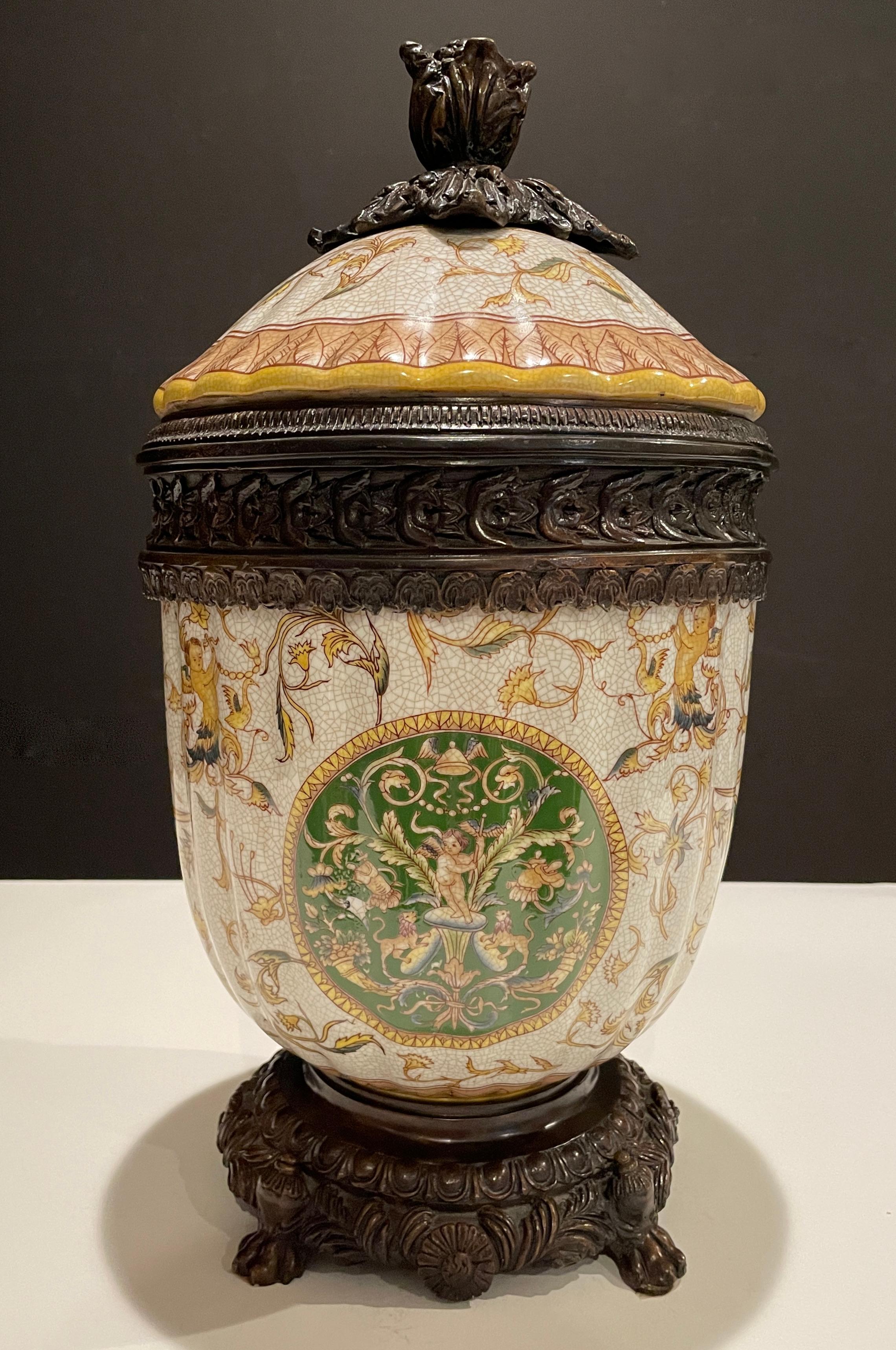 Bronze mounted ceramic covered urn. With Regency style green medallions and golden yellow borders, vines and leaves. Featuring winged cupids, putti, lions, cornucopia and early military elements.